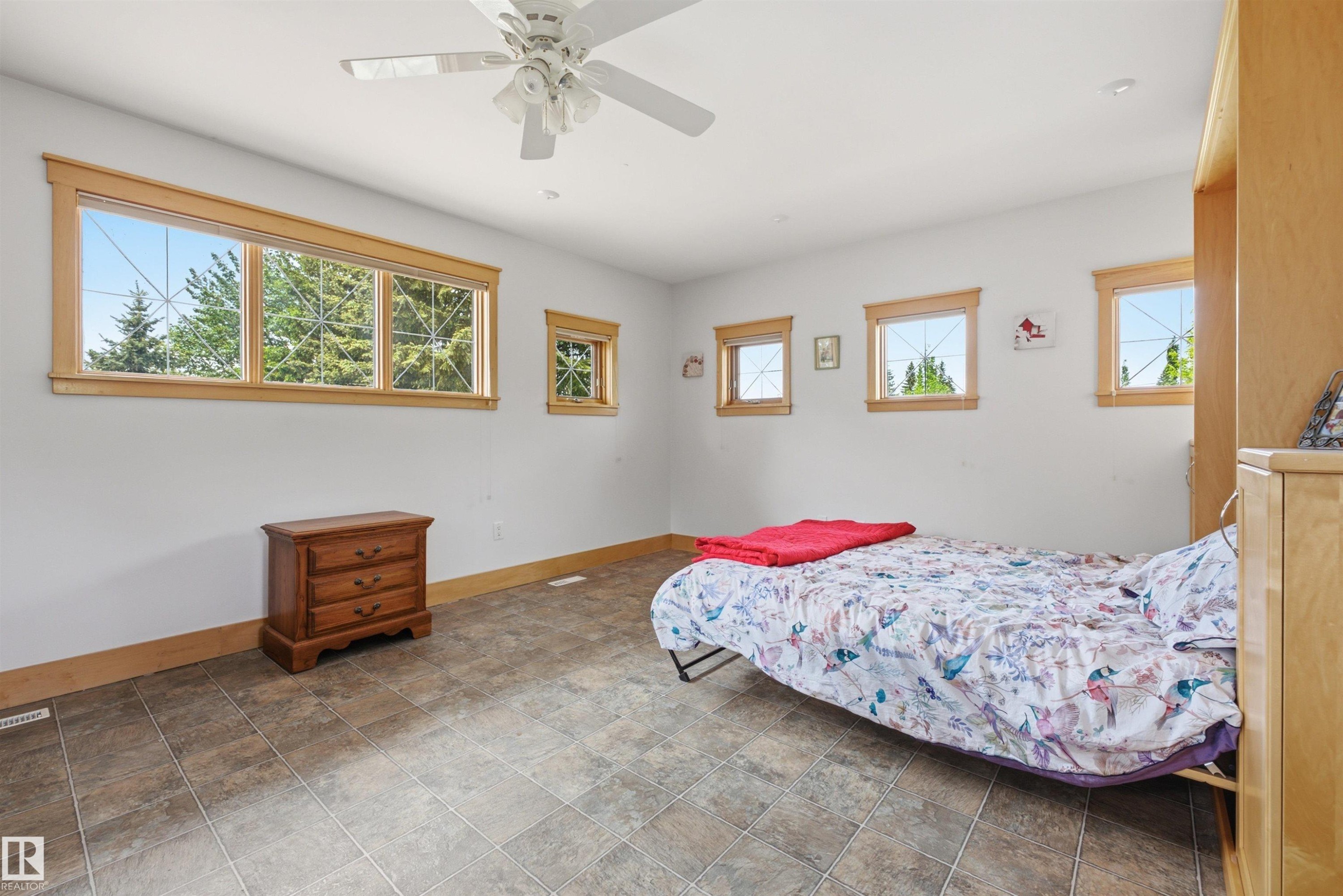 Spacious room featuring multiple windows with wood trim, a ceiling fan, and durable tile flooring - A38 Bernice Ave, Rural Leduc County, AB