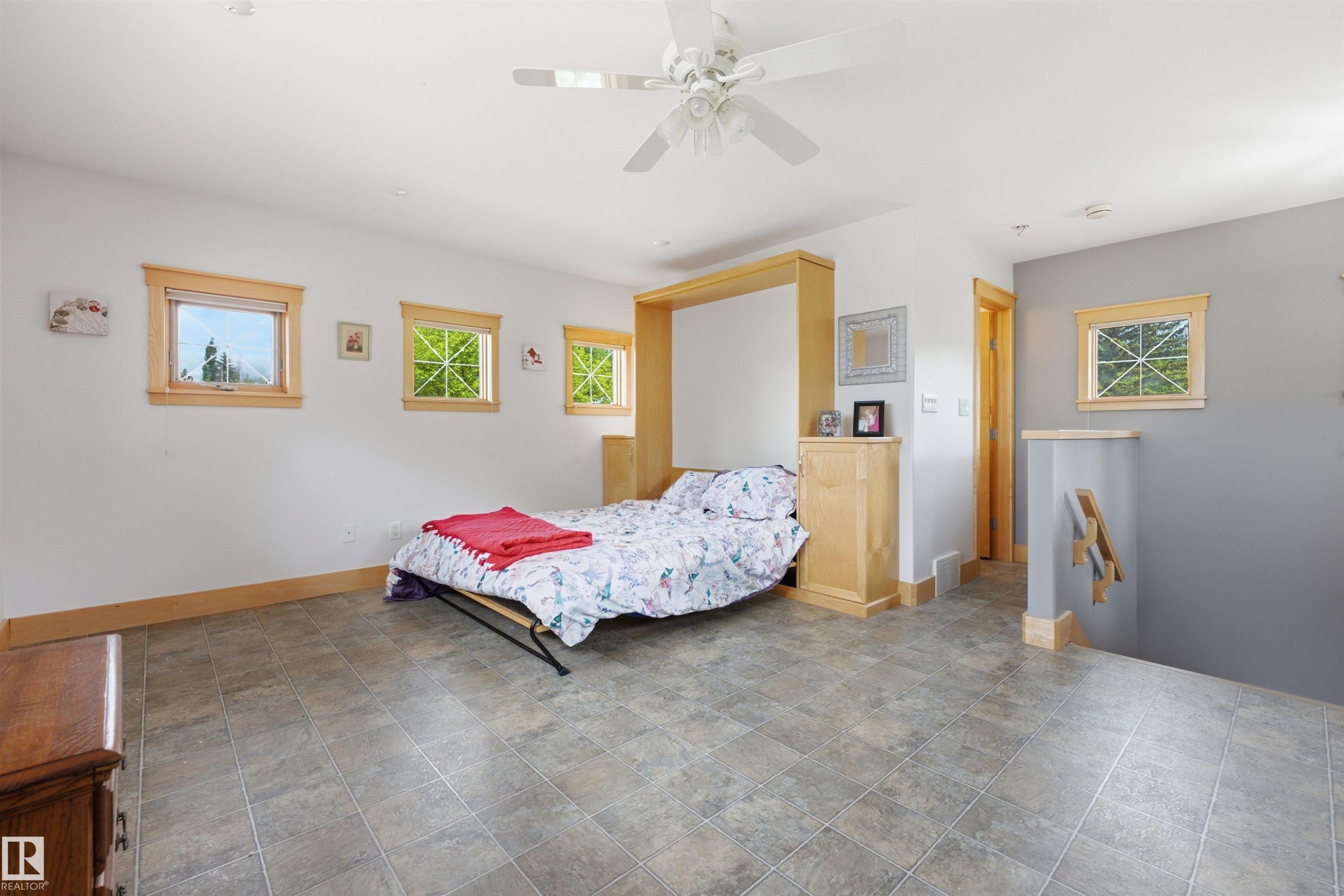 Spacious room featuring tile flooring, a ceiling fan, and multiple windows with wood trim - A38 Bernice Ave, Rural Leduc County, AB