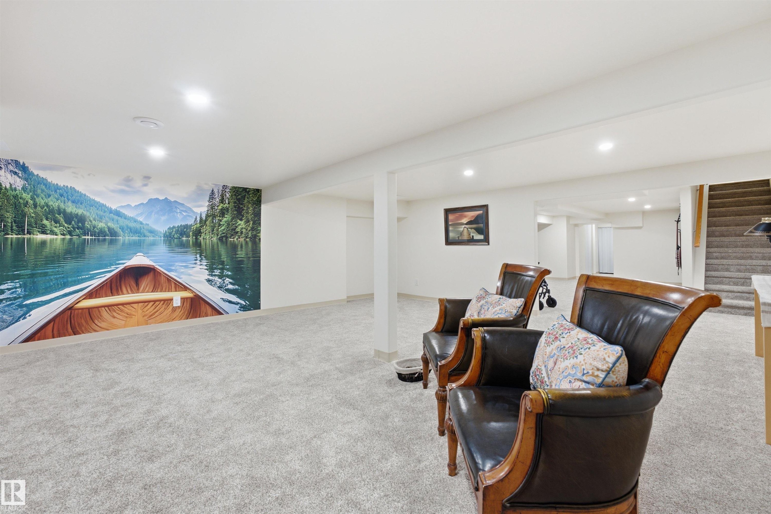 Spacious finished room featuring a scenic wall mural, light-colored carpeting, recessed lighting, and a visible staircase - A38 Bernice Ave, Rural Leduc County, AB