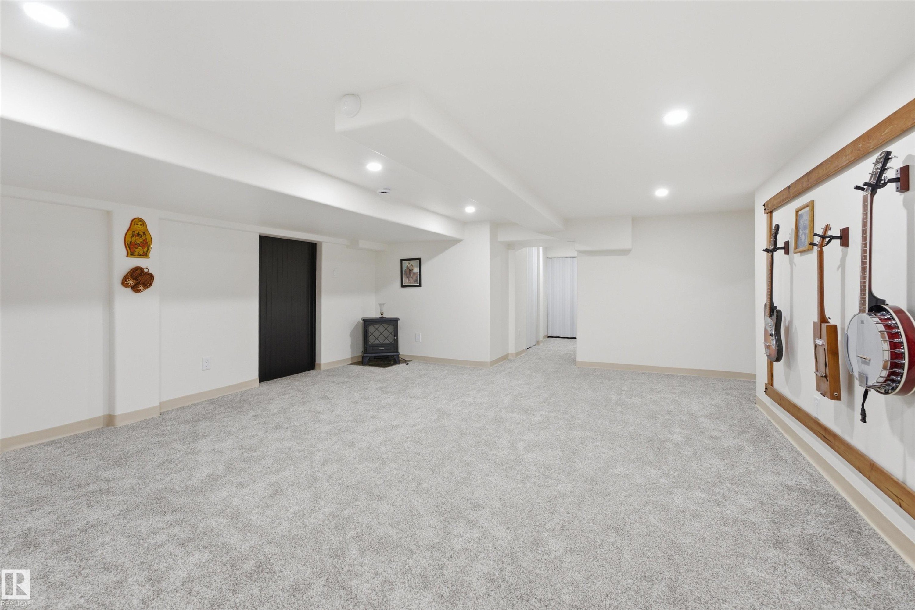 Finished lower level featuring light gray carpeting, recessed lighting, white walls, a black interior door, and a freestanding stove - A38 Bernice Ave, Rural Leduc County, AB