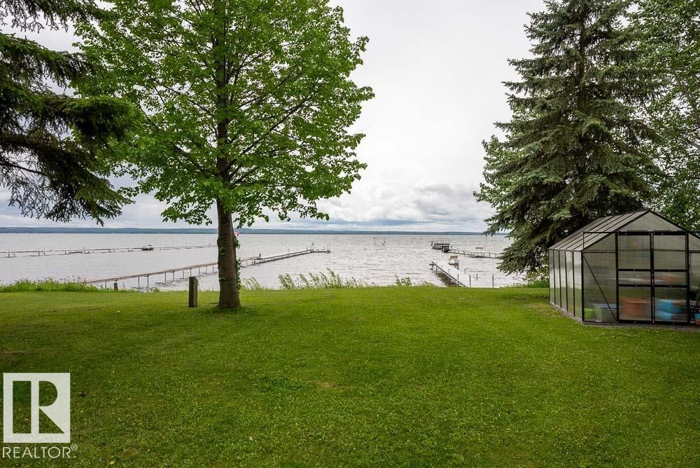Expansive green lawn sloping towards a body of water with multiple boat docks - A38 Bernice Ave, Rural Leduc County, AB