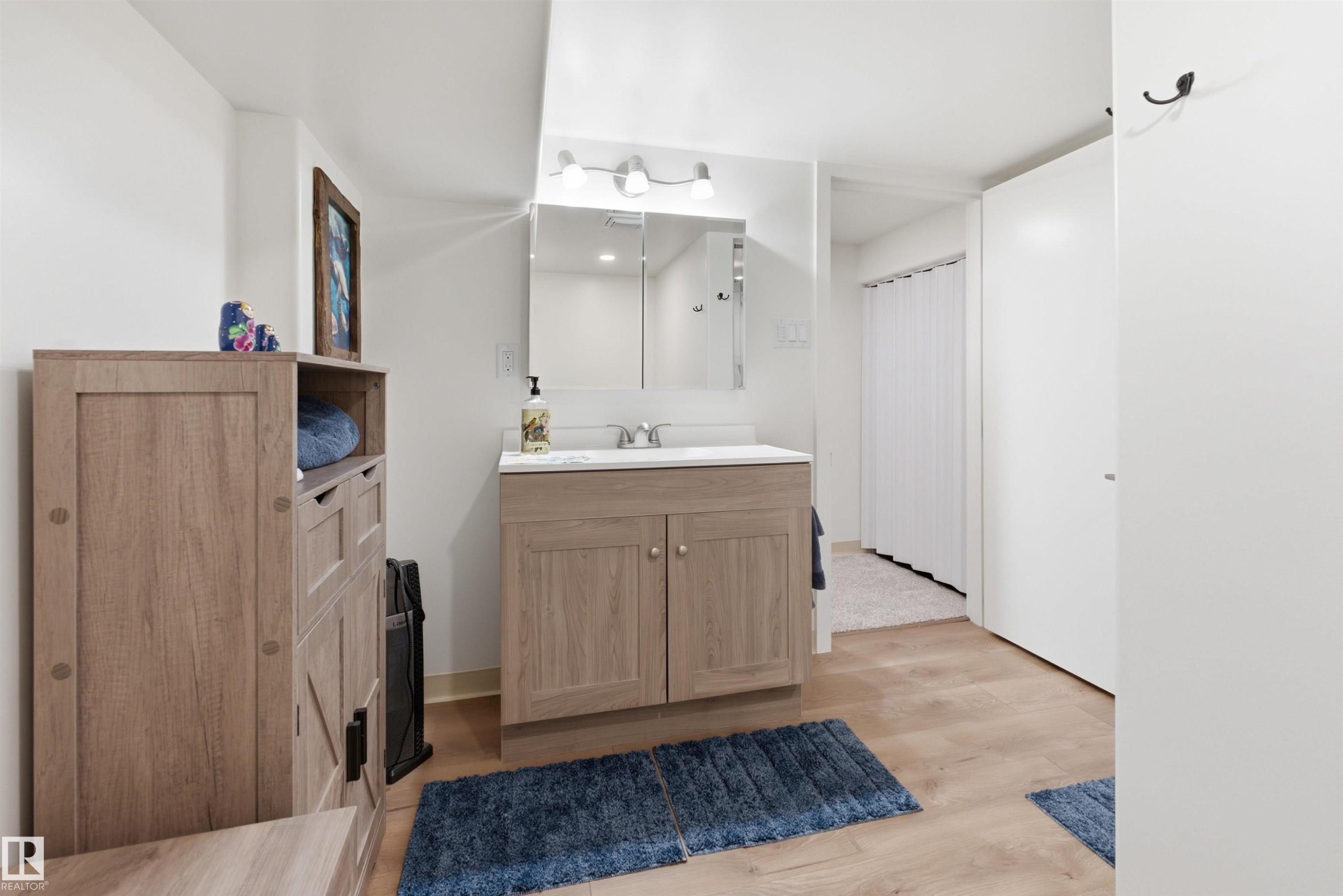 Bathroom featuring a wood-finish vanity with a white countertop and integrated sink, mirrored medicine cabinet, and overhead vanity light fixture - A38 Bernice Ave, Rural Leduc County, AB