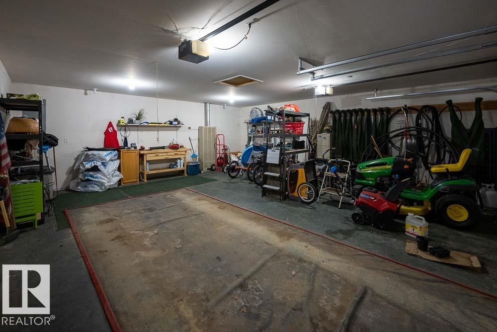 Spacious garage featuring concrete flooring, track lighting, an overhead garage door opener, and integrated wall shelving - A38 Bernice Ave, Rural Leduc County, AB