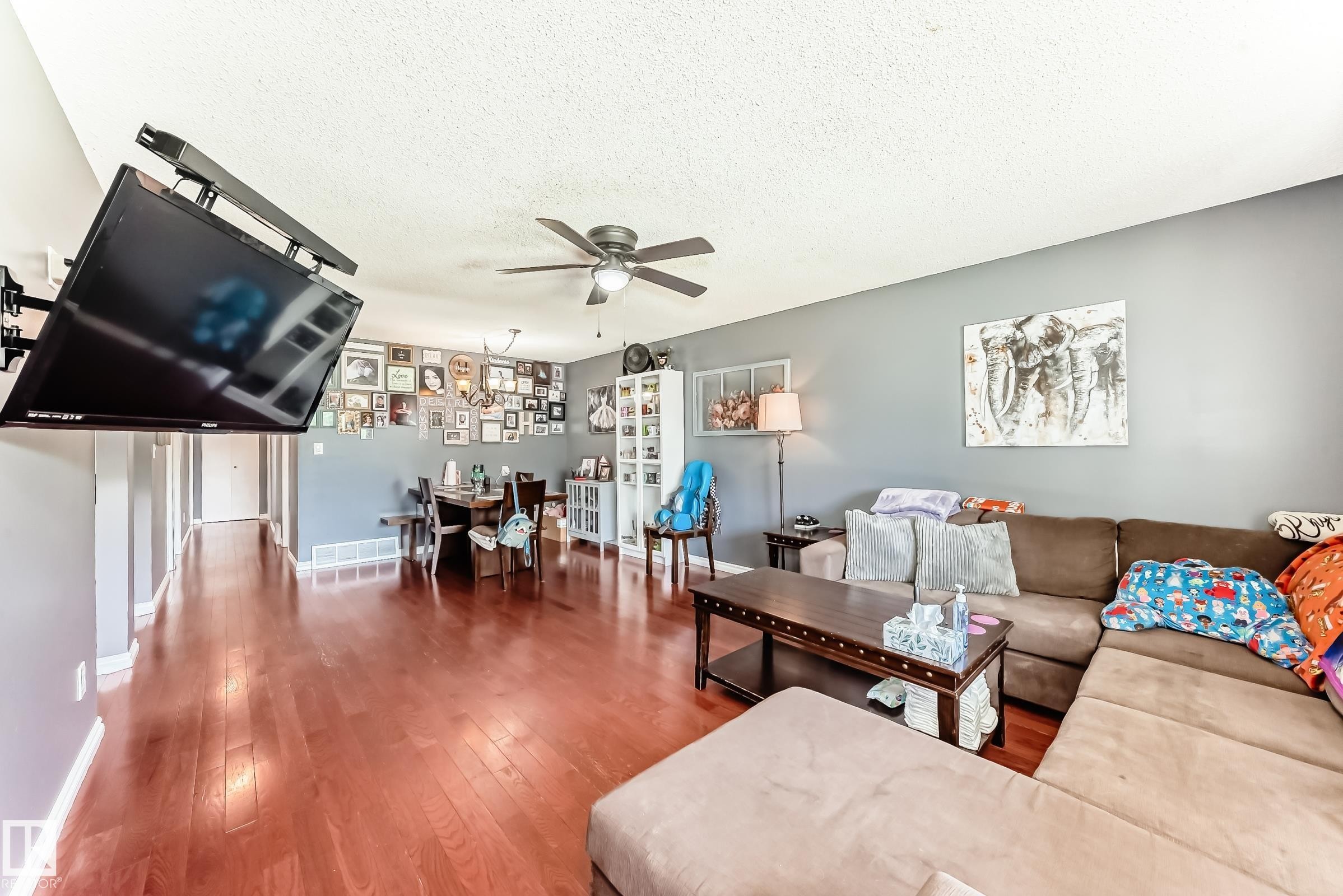 Open-concept living area featuring rich wood-finish flooring, a neutral wall color, and a ceiling fan with integrated lighting - 5106 19 Avenue, Edmonton, AB