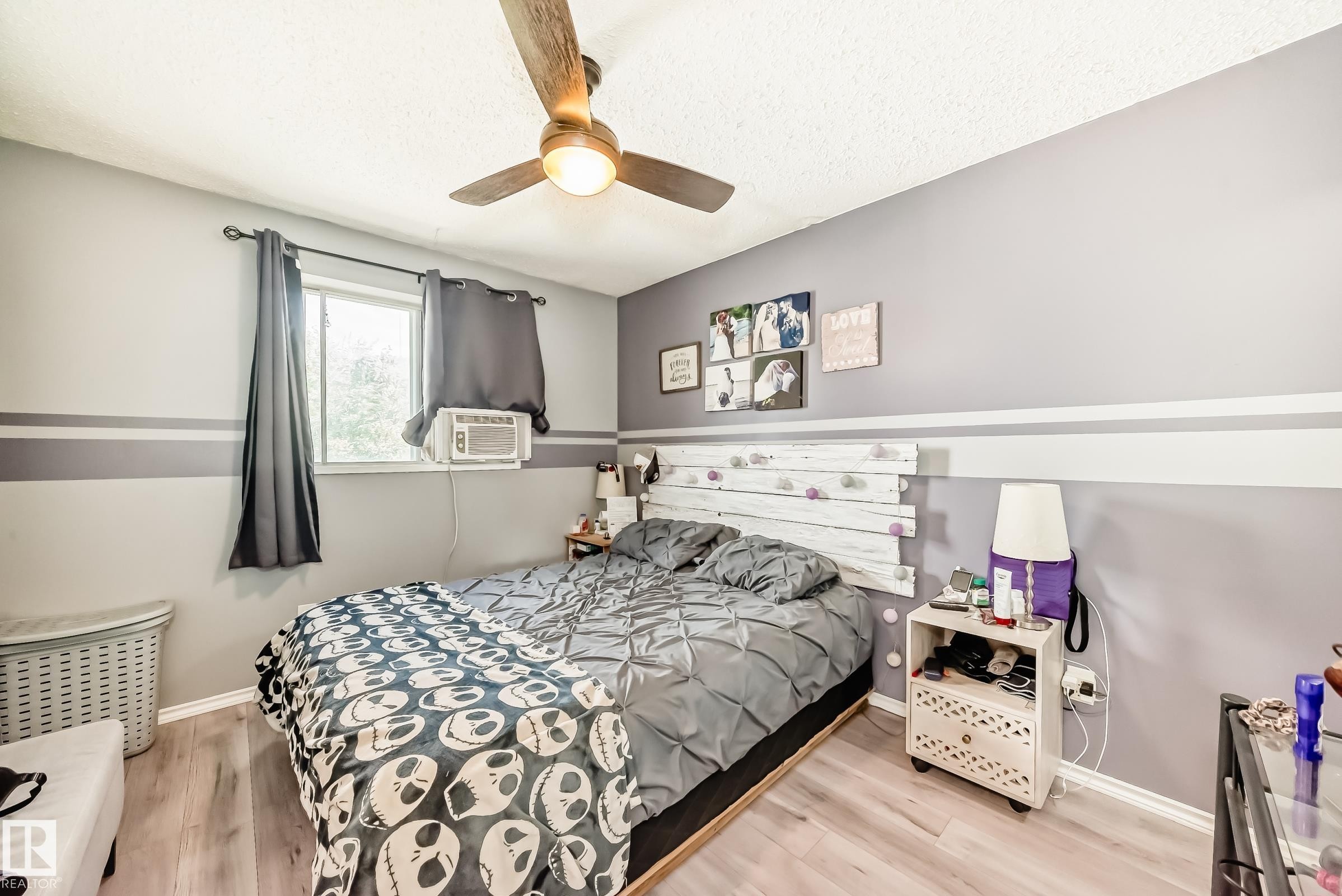 Bedroom featuring wood-finish flooring, a window with dark curtains, and a ceiling fan with integrated lighting - 5106 19 Avenue, Edmonton, AB