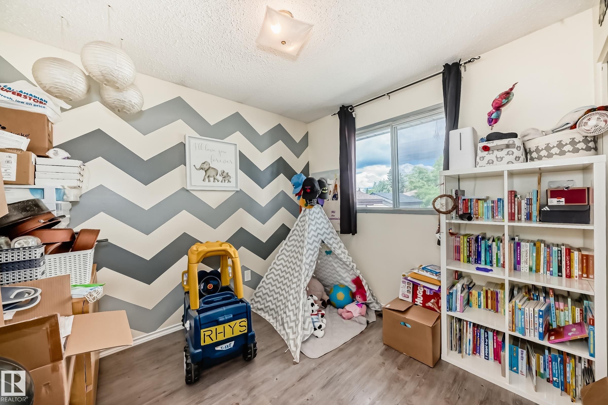 Room featuring chevron accent wall, wood-finish flooring, and a large window with exterior views - 5106 19 Avenue, Edmonton, AB