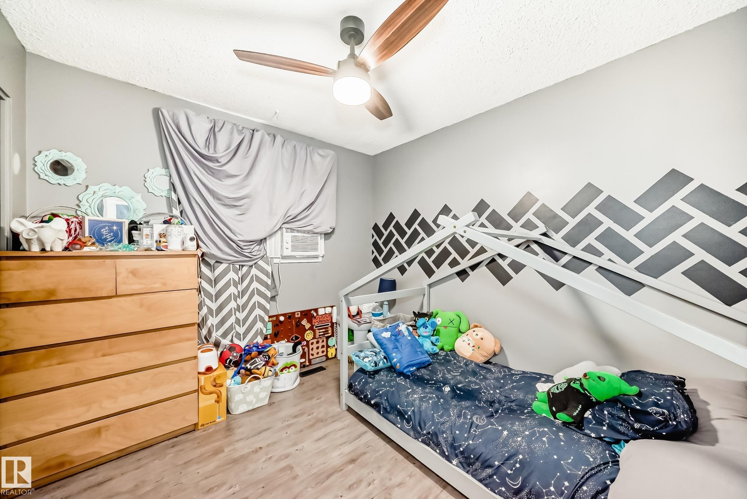 Room featuring wood-finish flooring, a ceiling fan with integrated lighting, and a window with a room air conditioning unit - 5106 19 Avenue, Edmonton, AB