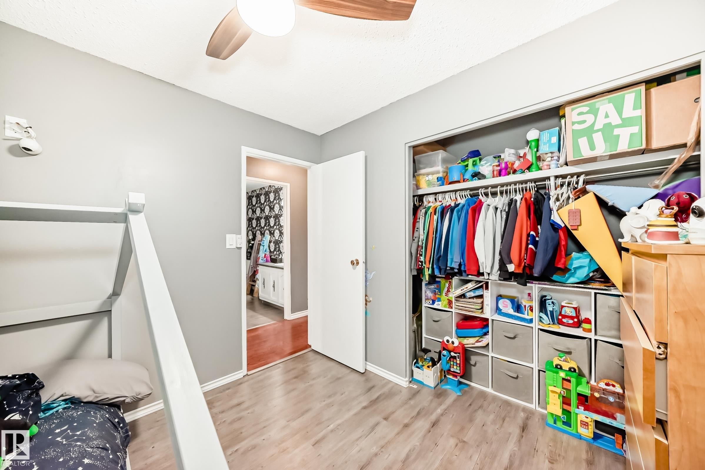 Spacious room featuring wood-finish flooring, a ceiling fan with integrated lighting, and a built-in closet with shelving - 5106 19 Avenue, Edmonton, AB