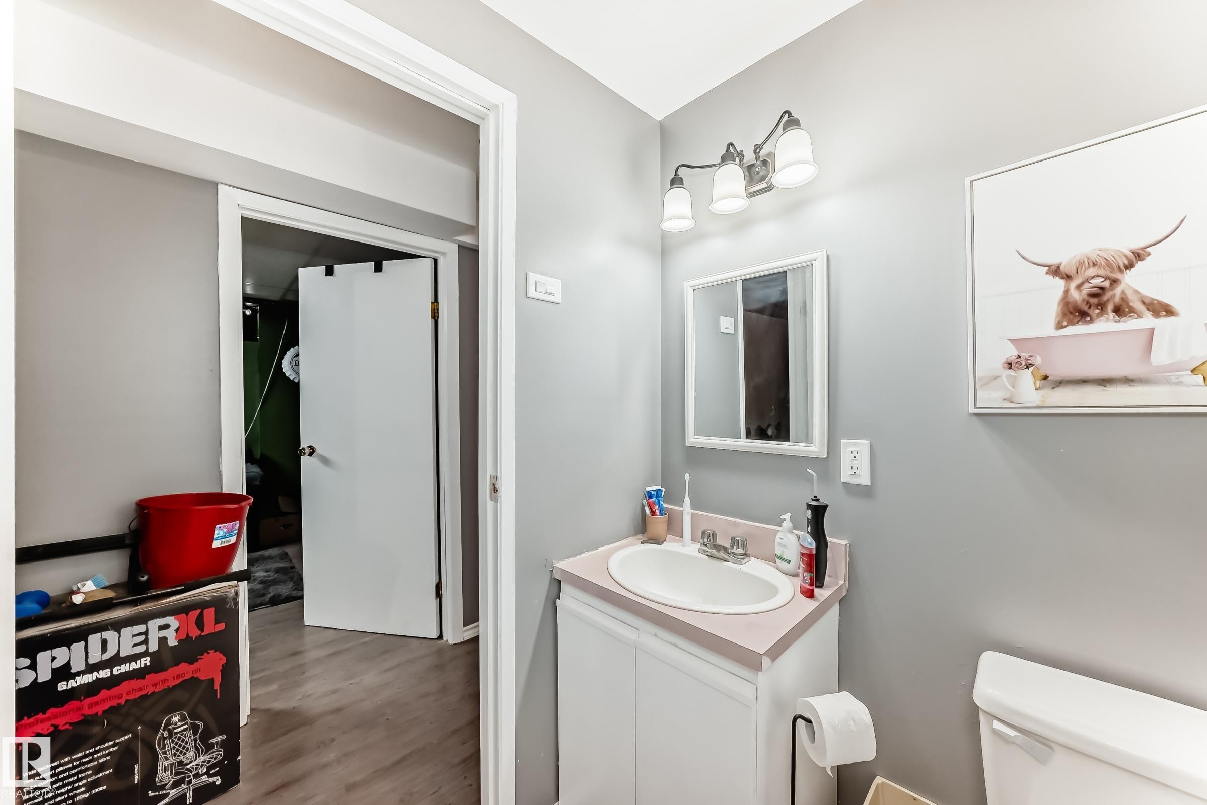 Bathroom featuring a white vanity cabinet with an integrated sink and light-toned countertop, a wall-mounted mirror, and a three-light fixture - 5106 19 Avenue, Edmonton, AB