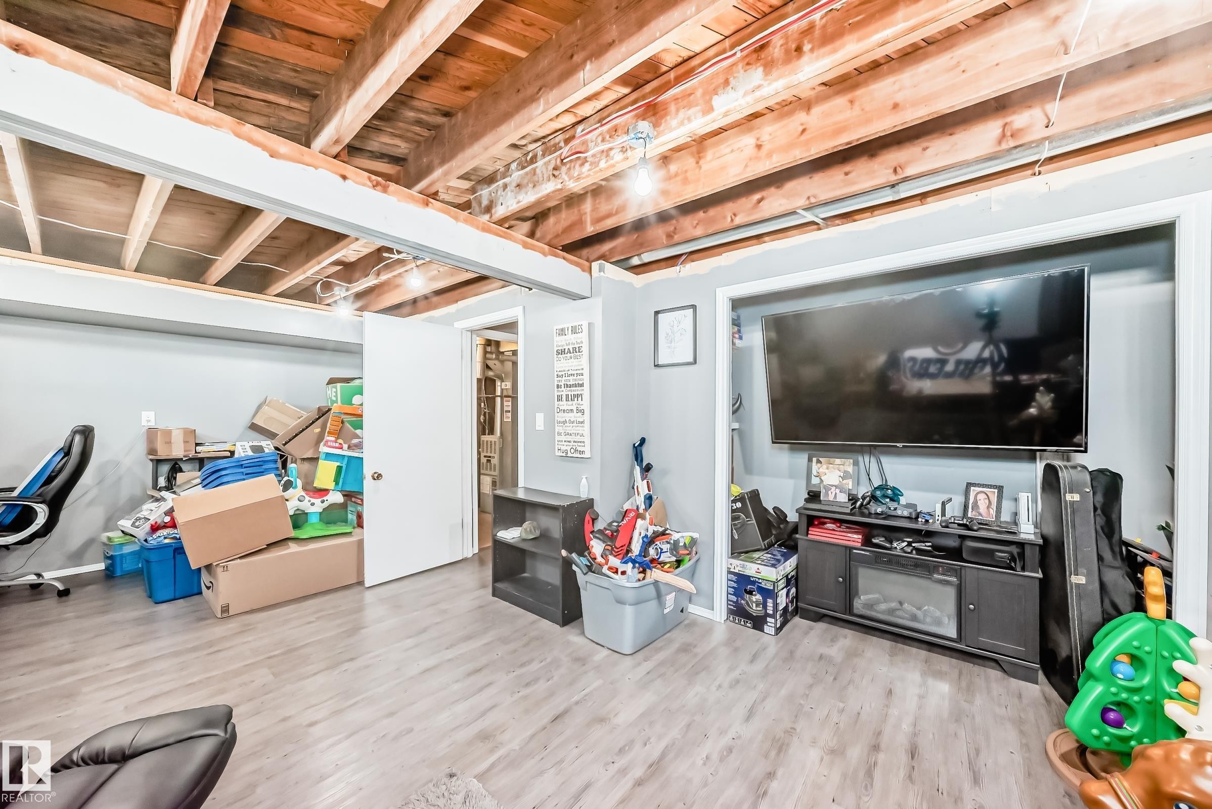 Exposed wooden ceiling beams and light wood-finish flooring define this versatile lower-level space - 5106 19 Avenue, Edmonton, AB