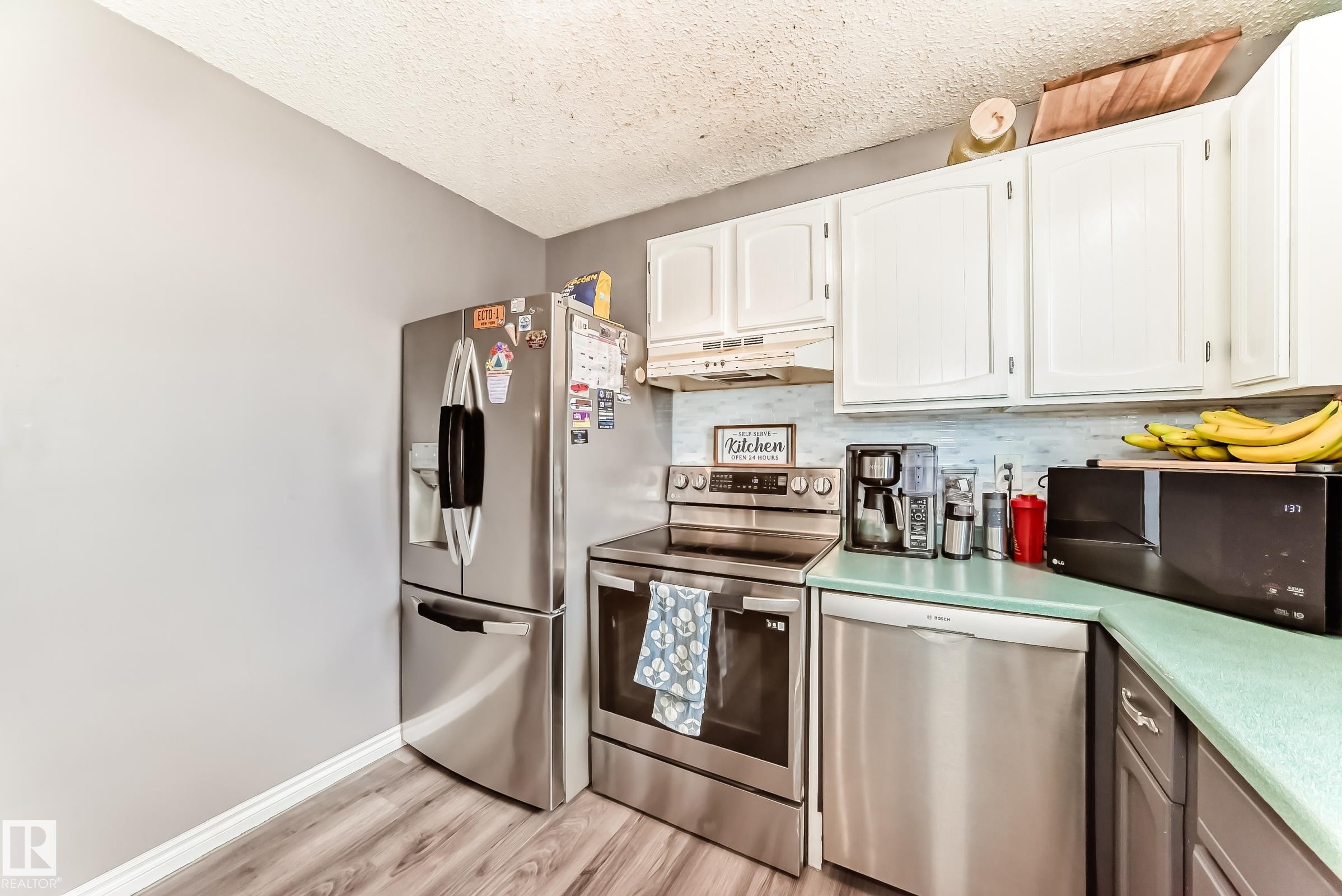 Kitchen featuring white upper cabinetry, teal countertops, a light blue tile backsplash, and wood-finish flooring - 5106 19 Avenue, Edmonton, AB