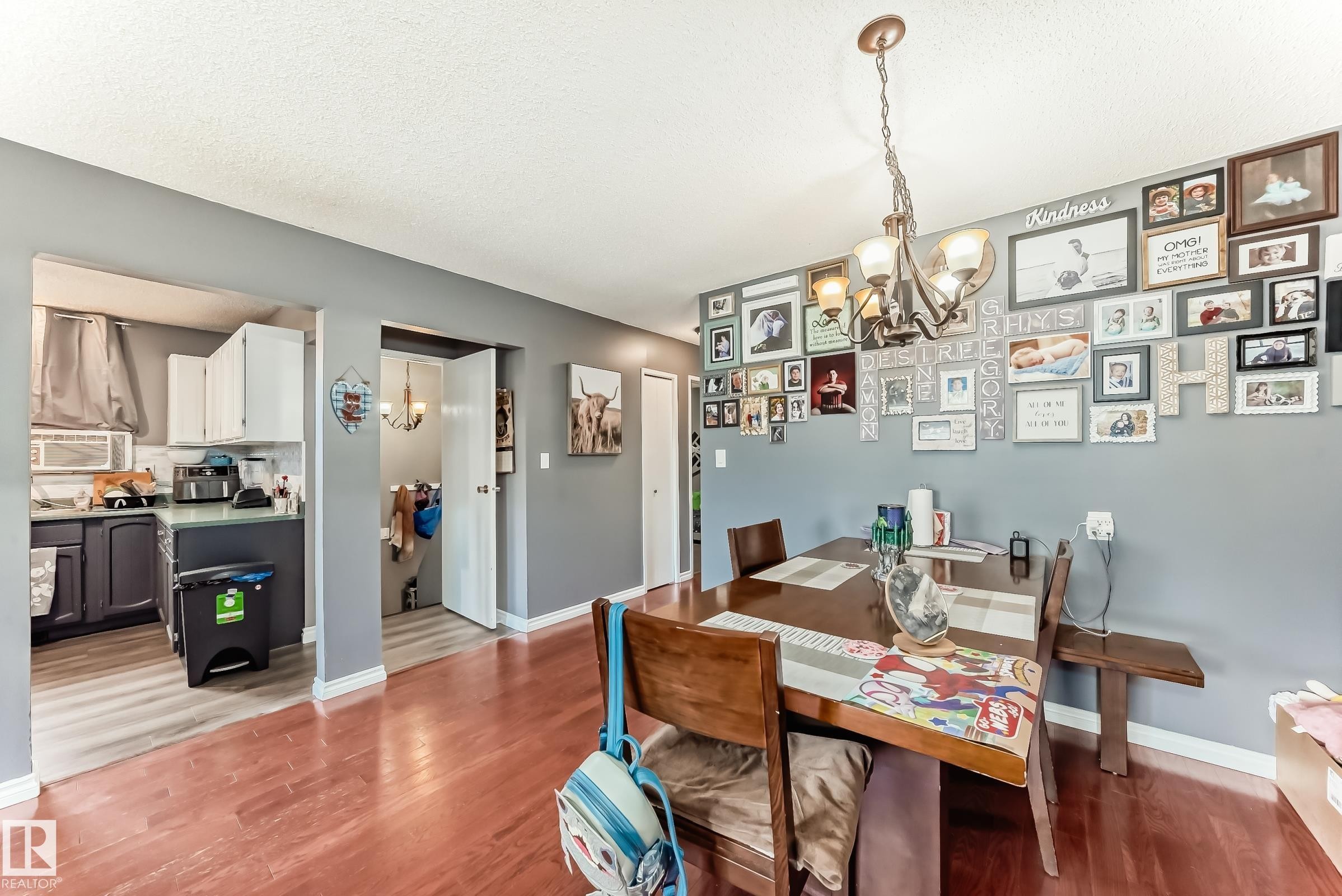 Dining area featuring wood-finish flooring, a decorative chandelier, and a framed opening to the kitchen - 5106 19 Avenue, Edmonton, AB