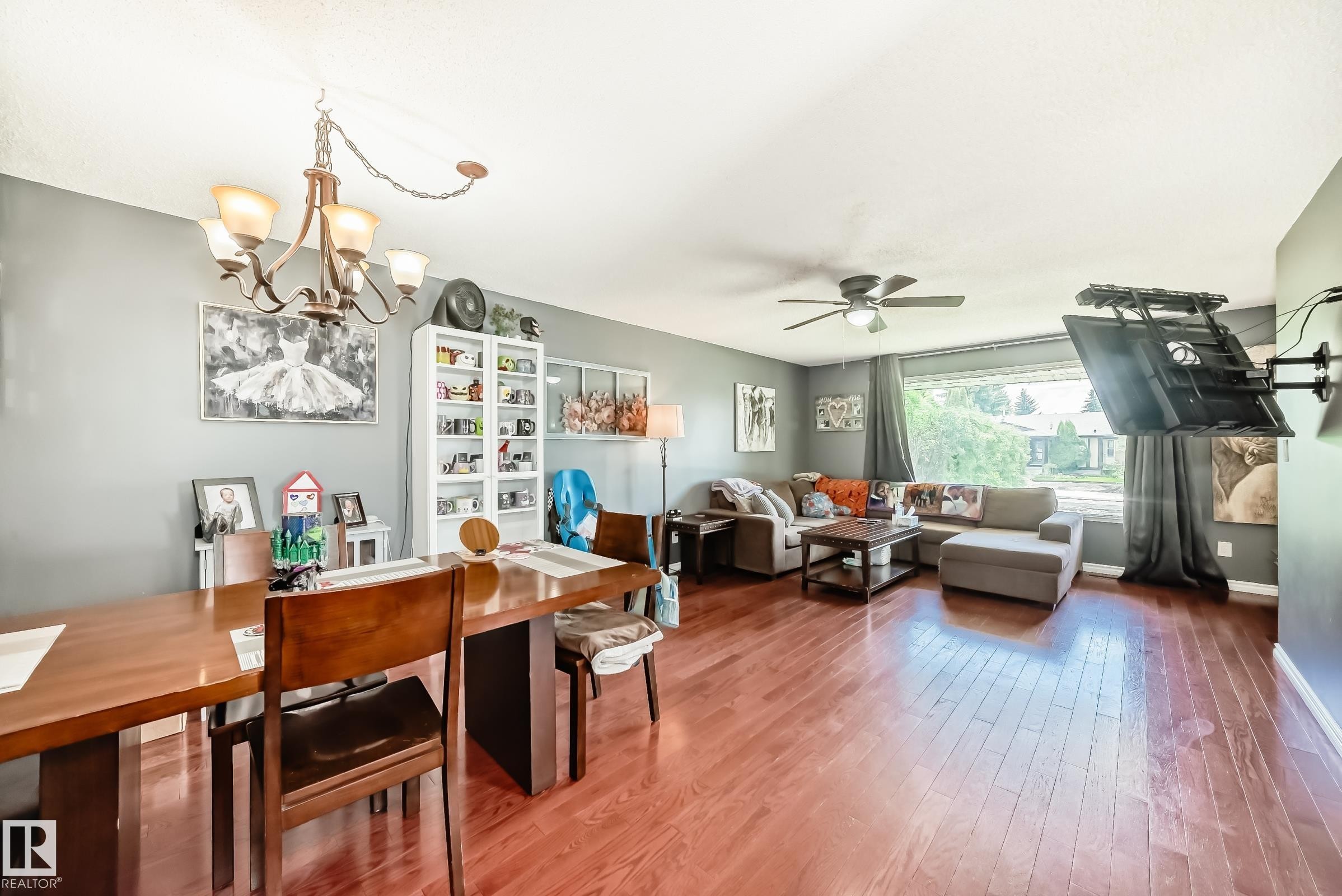 Open-concept living space featuring wood-finish flooring, a contemporary chandelier, and a ceiling fan - 5106 19 Avenue, Edmonton, AB