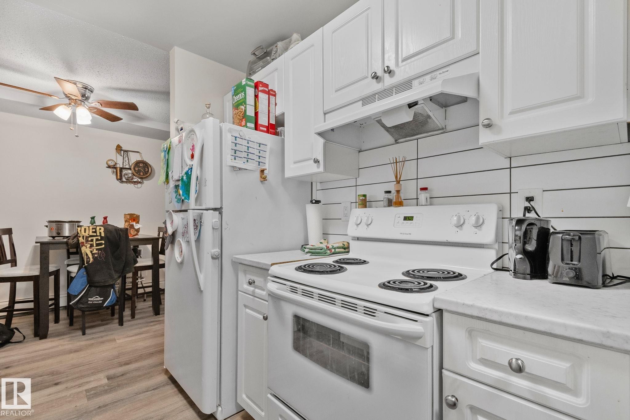 Kitchen featuring white cabinetry, white countertops, white electric range, white refrigerator, and a white shiplap-style backsplash - 115 4608 52 Avenue, Stony Plain, AB