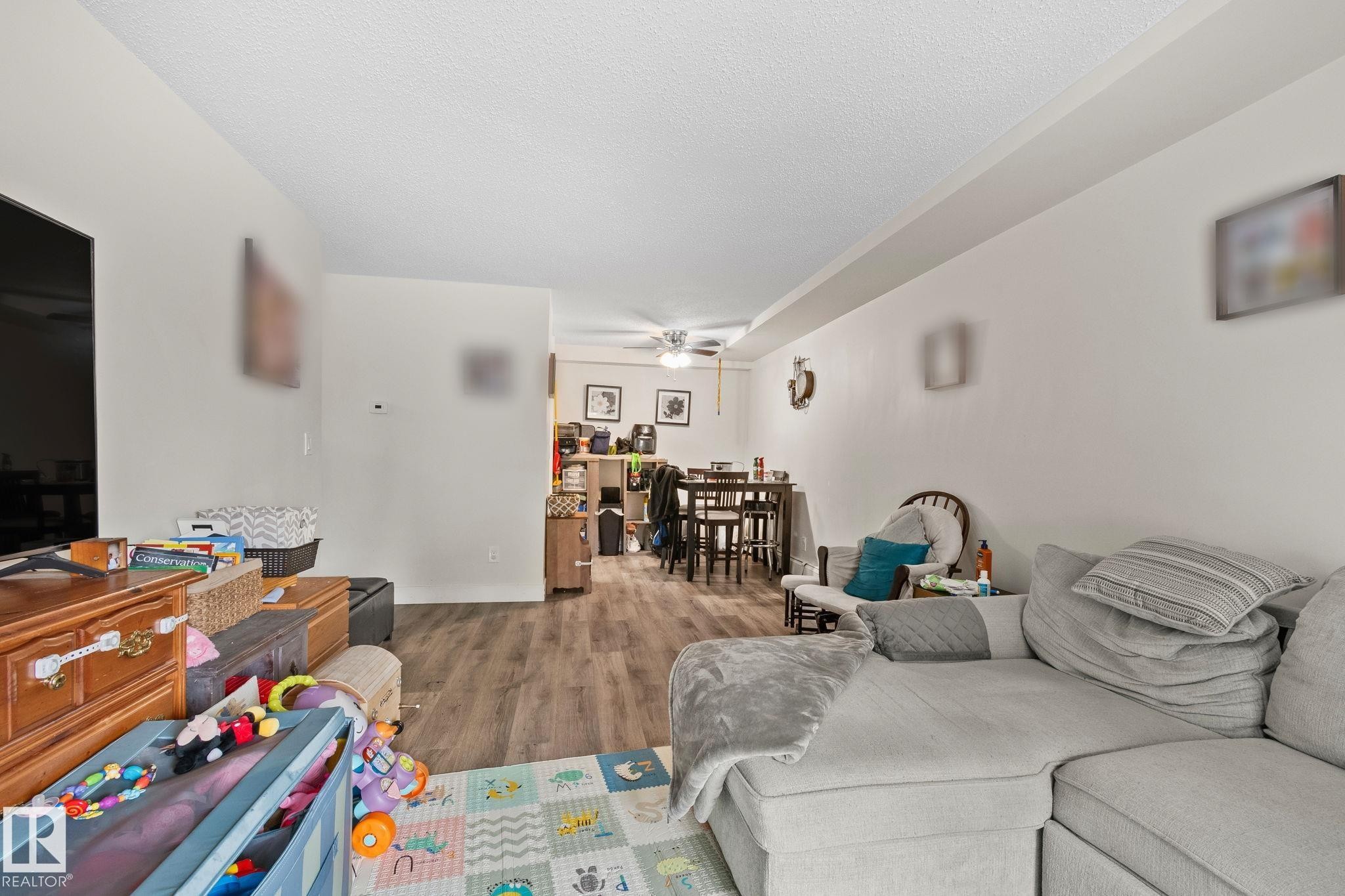Spacious living area featuring wood-finish flooring, crisp white walls, and an open layout - 115 4608 52 Avenue, Stony Plain, AB