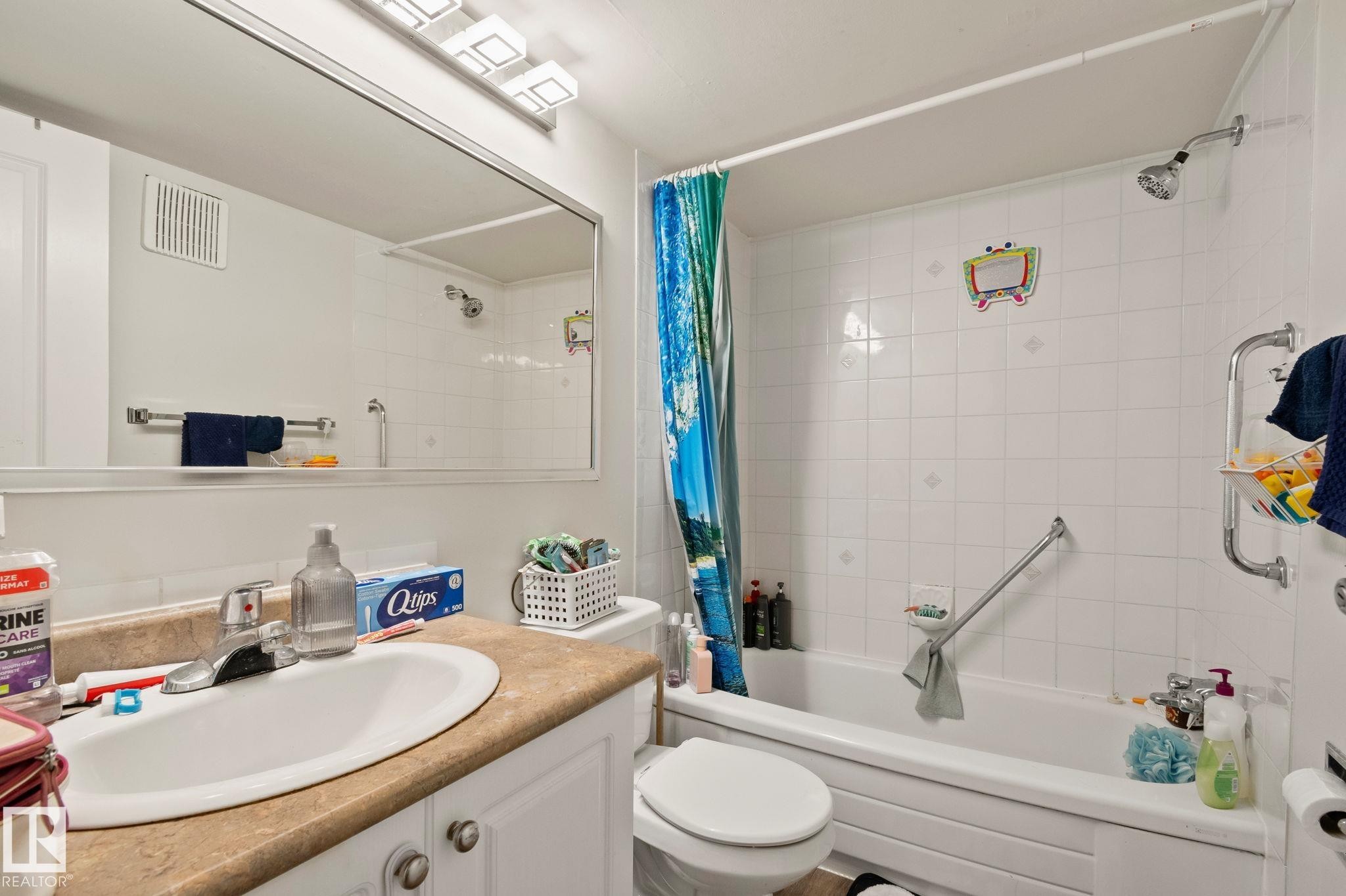 Bathroom featuring a vanity with an integrated sink, a rectangular mirror, and a combination shower-bathtub with white tiled walls - 115 4608 52 Avenue, Stony Plain, AB