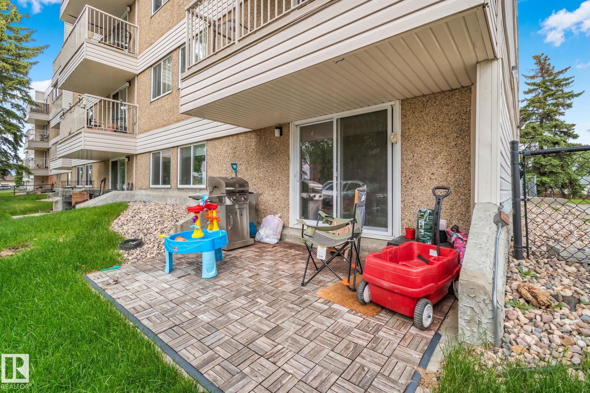 Ground-level patio featuring wood-finish paver tiles and direct access via sliding glass doors - 115 4608 52 Avenue, Stony Plain, AB