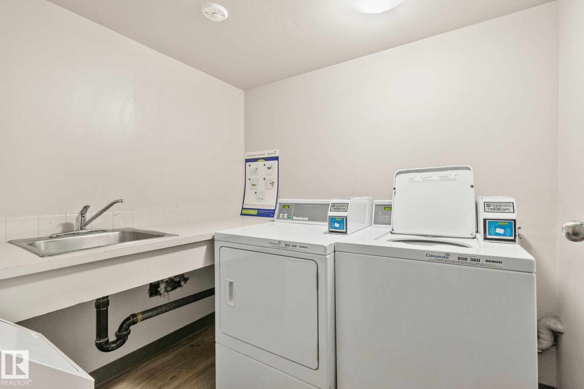 Laundry area featuring a utility sink, light-toned countertop, and two large-capacity washing machines - 115 4608 52 Avenue, Stony Plain, AB