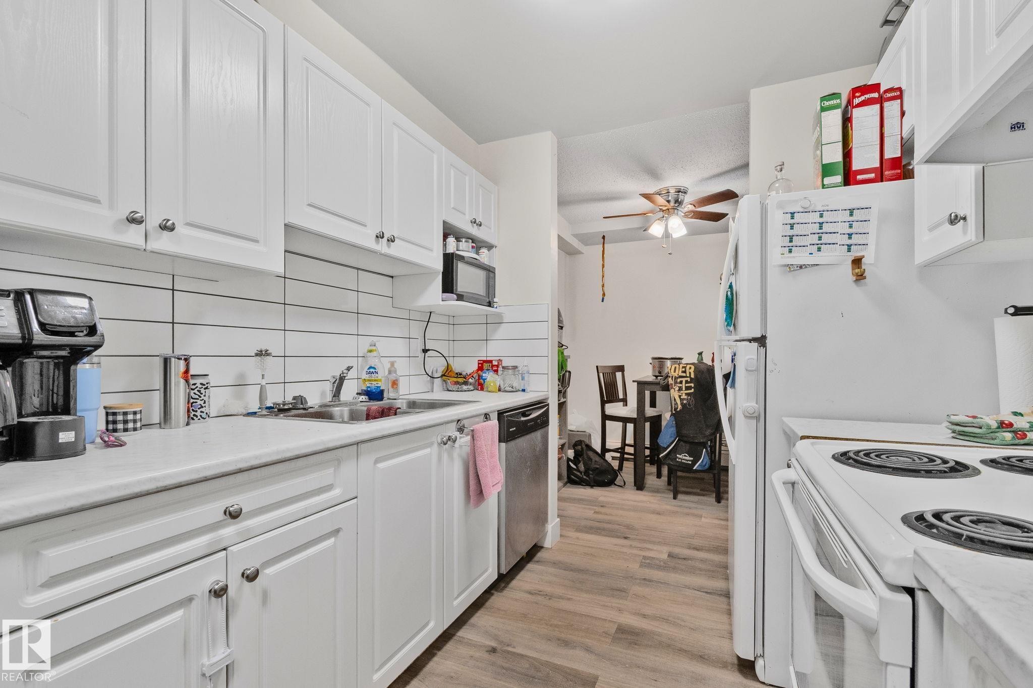 Kitchen featuring white cabinetry, a single basin stainless steel sink, a dishwasher, a microwave, and a white refrigerator - 115 4608 52 Avenue, Stony Plain, AB