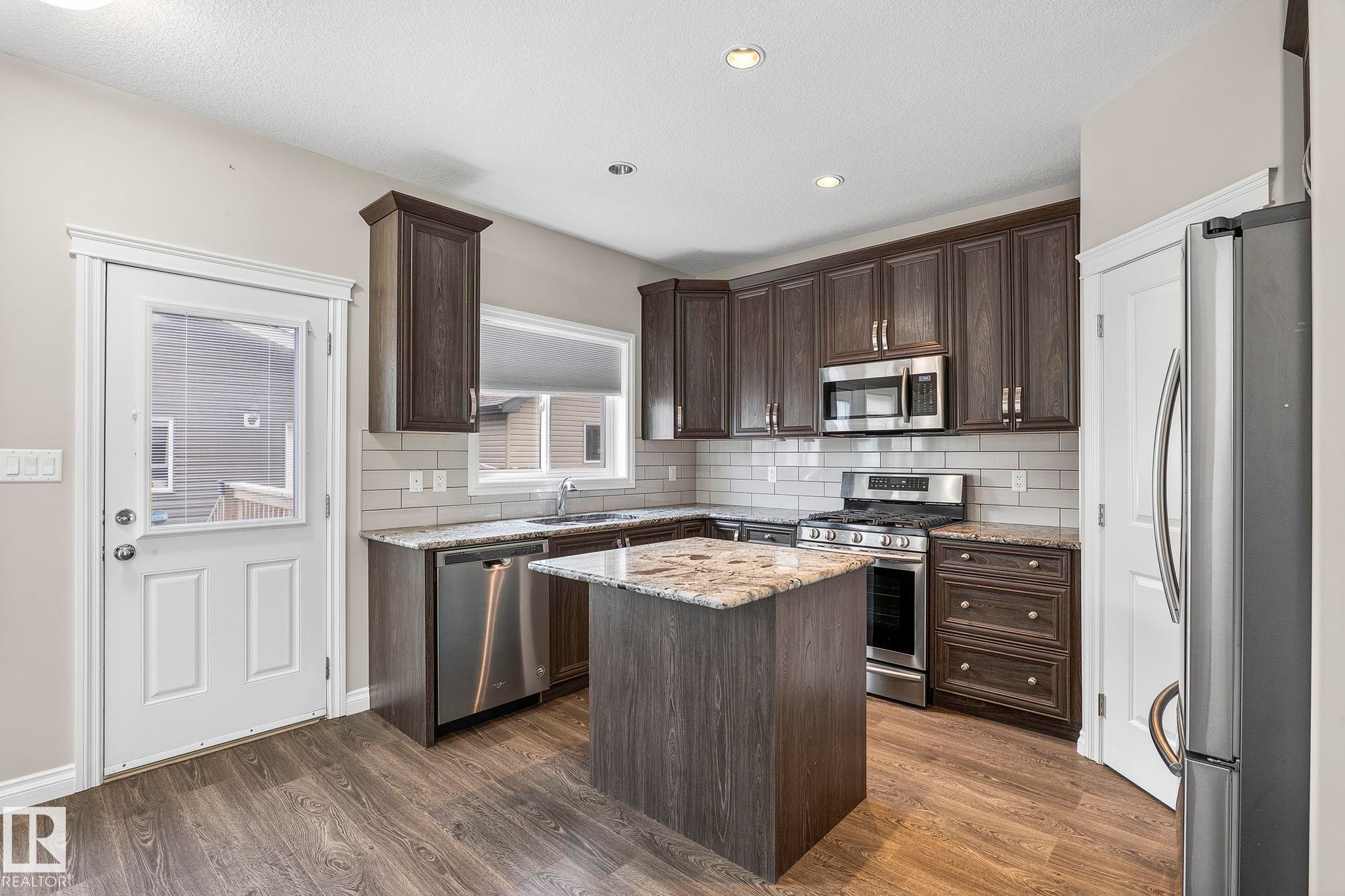 Modern kitchen featuring dark wood-finish cabinetry, granite countertops, and stainless steel appliances - 6927 Cardinal Wynd Sw, Edmonton, AB - Indoor Photo Showing Kitchen With Upgraded Kitchen
