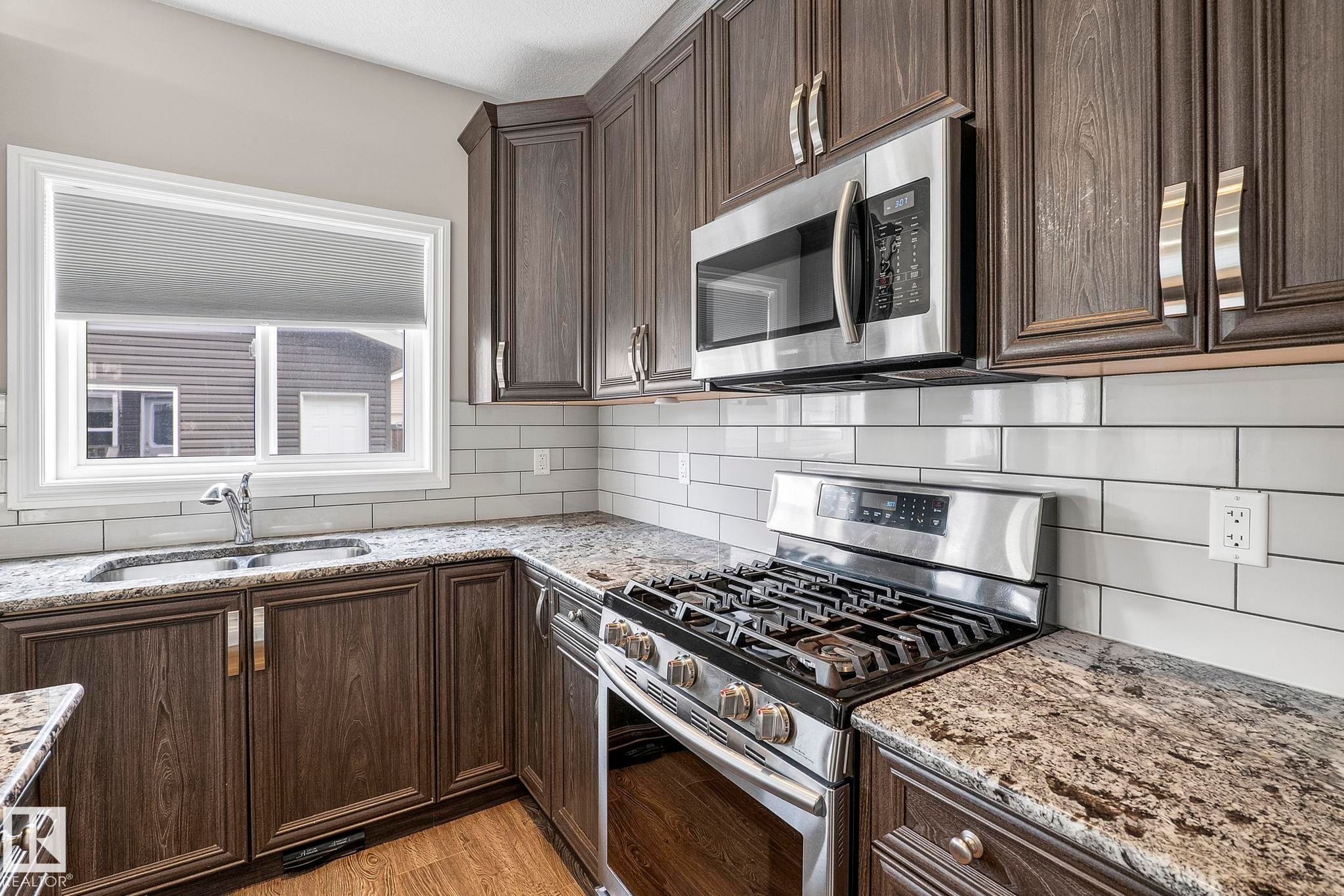 Kitchen featuring wood-finish cabinetry, speckled countertops, and a white subway tile backsplash - 6927 Cardinal Wynd Sw, Edmonton, AB - Indoor Photo Showing Kitchen With Double Sink With Upgraded Kitchen