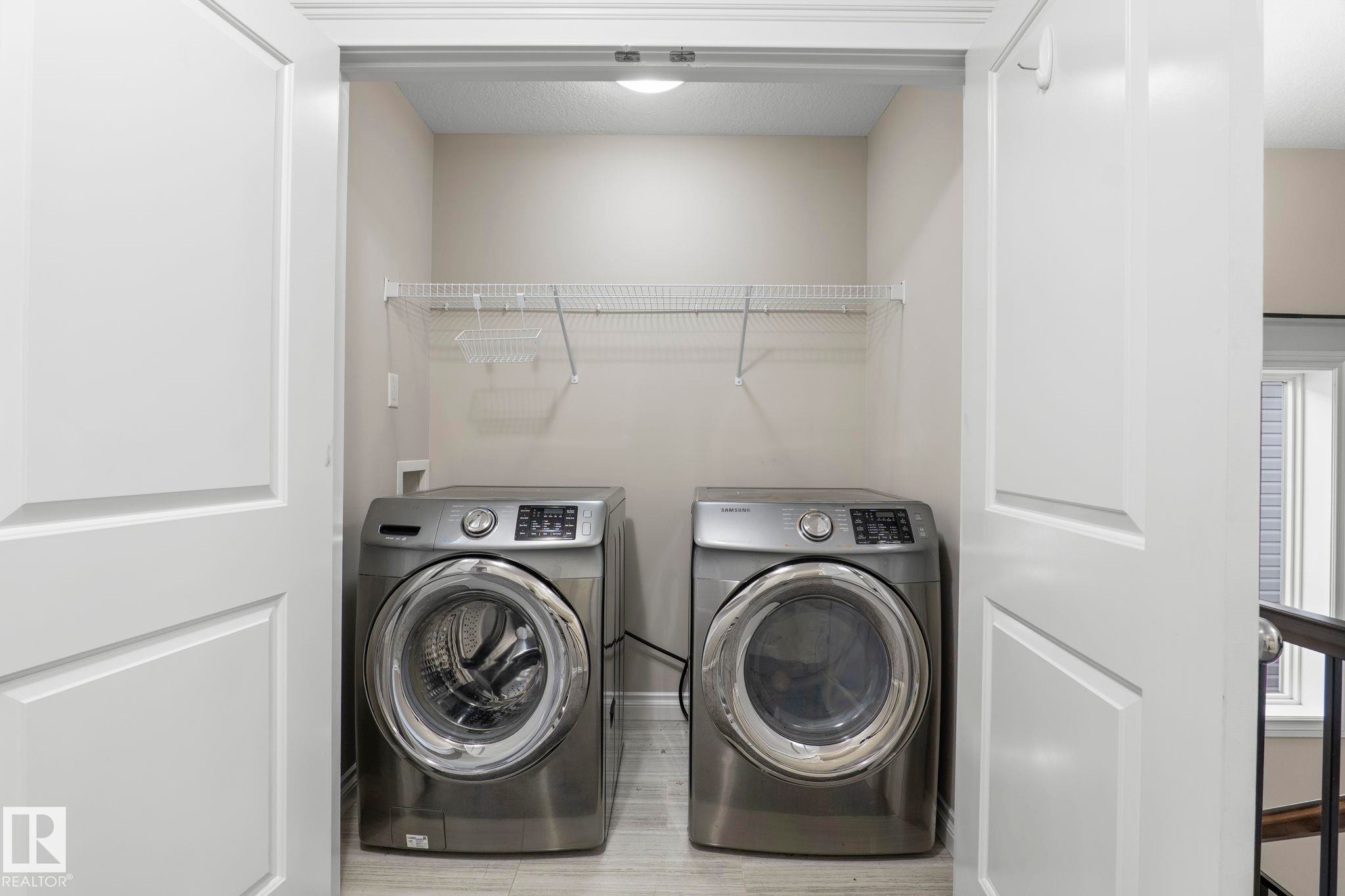 Dedicated laundry area with front-loading washer and dryer, featuring overhead wire shelving and light-toned flooring - 6927 Cardinal Wynd Sw, Edmonton, AB - Indoor Photo Showing Laundry Room