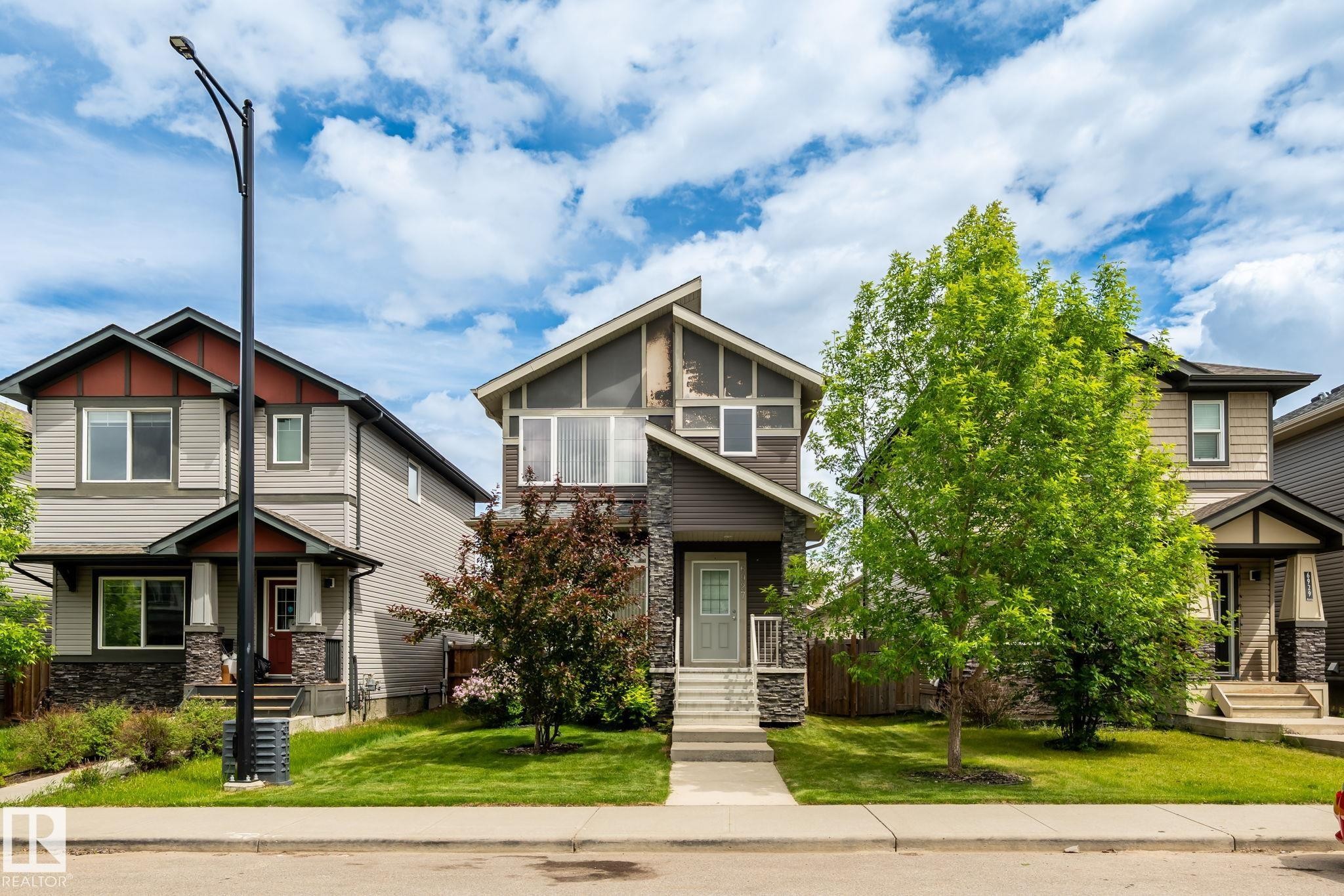 Two-story home with a stone and siding exterior, featuring a covered front porch, an asymmetrical roofline, and a manicured front lawn - 6927 Cardinal Wynd Sw, Edmonton, AB - Outdoor With Facade