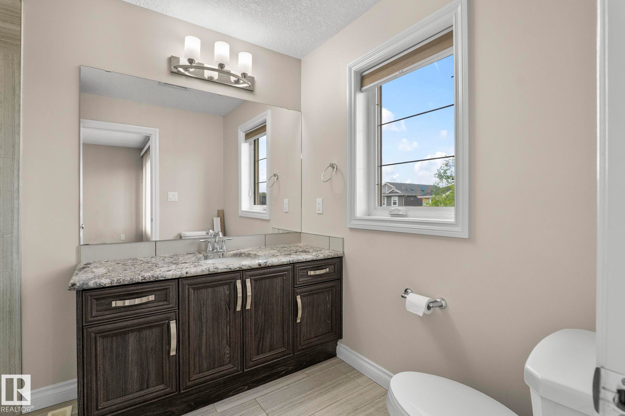Bathroom vanity featuring a granite countertop, wood-finish cabinetry, and a large wall mirror - 6927 Cardinal Wynd Sw, Edmonton, AB - Indoor Photo Showing Bathroom