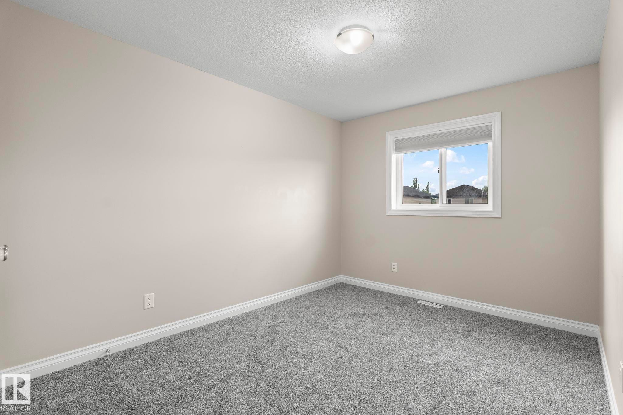 Carpeted room featuring a double-paned window, neutral wall paint, white baseboards, and a flush-mount ceiling light - 6927 Cardinal Wynd Sw, Edmonton, AB - Indoor Photo Showing Other Room