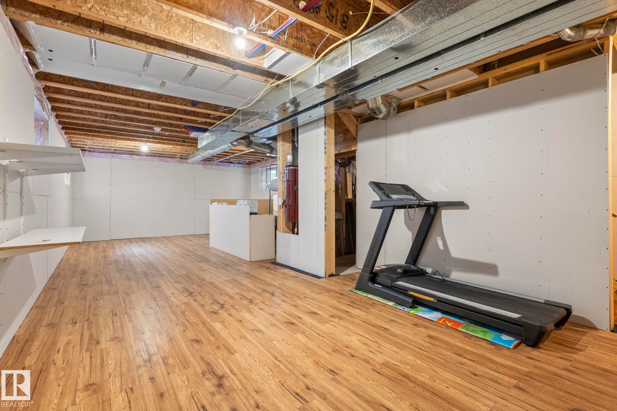 Finished lower level featuring wood-finish flooring, exposed ceiling joists, and partial drywall - 6927 Cardinal Wynd Sw, Edmonton, AB - Indoor Photo Showing Basement