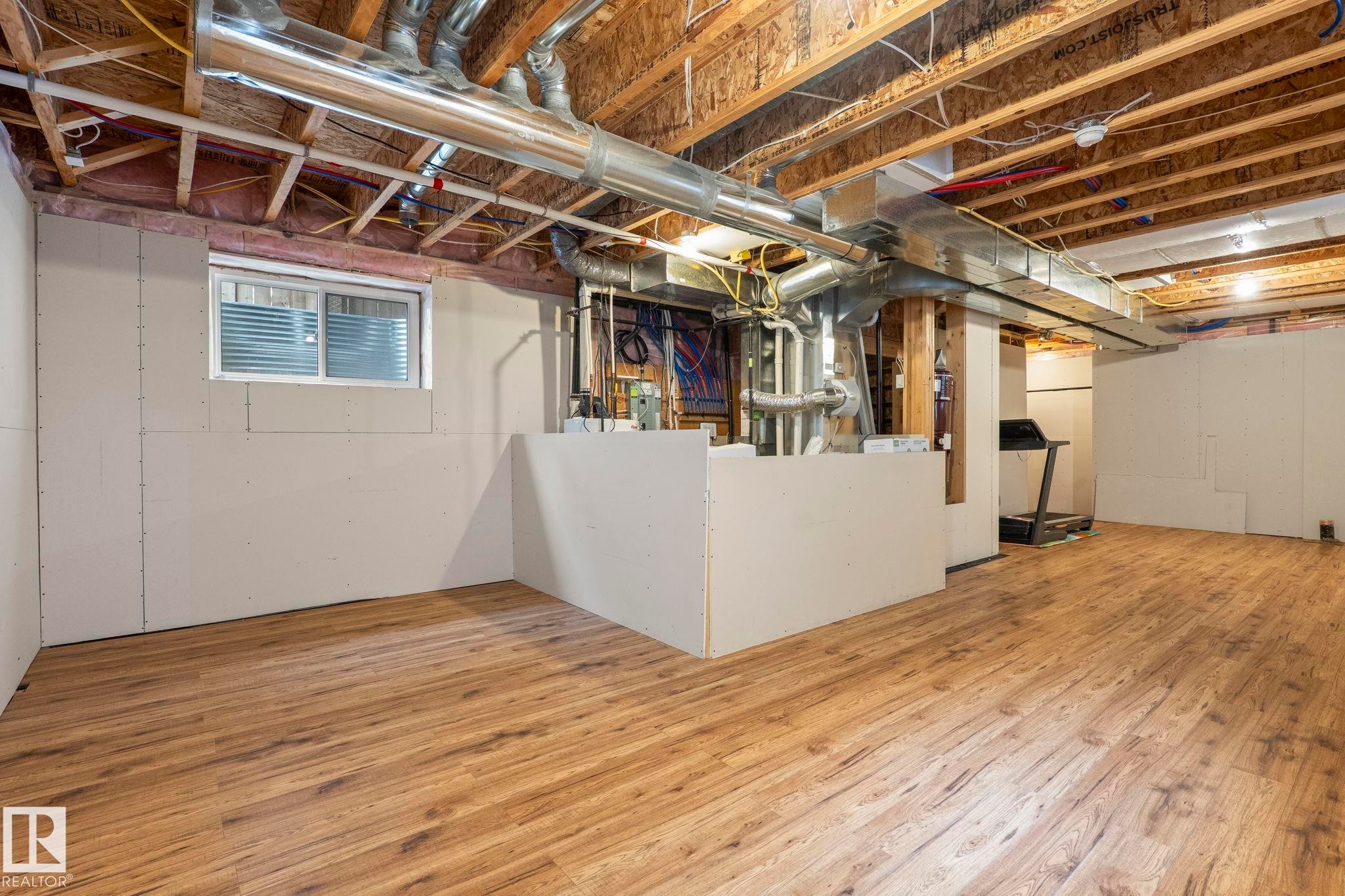 Lower level featuring wood-finish flooring, a window, and exposed ceiling joists - 6927 Cardinal Wynd Sw, Edmonton, AB - Indoor Photo Showing Basement