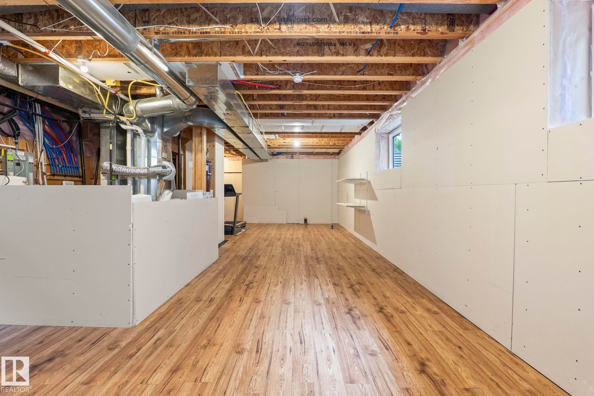 Lower level space featuring wood-finish flooring, exposed ceiling joists, and partial drywall installation - 6927 Cardinal Wynd Sw, Edmonton, AB - Indoor Photo Showing Basement