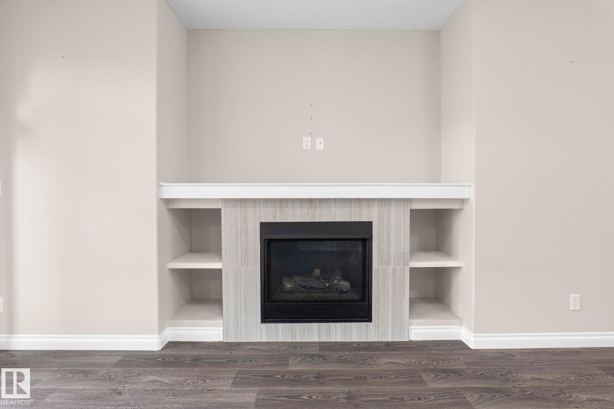 Fireplace feature wall with integrated shelving, tile surround, and wood-finish flooring - 6927 Cardinal Wynd Sw, Edmonton, AB - Indoor With Fireplace