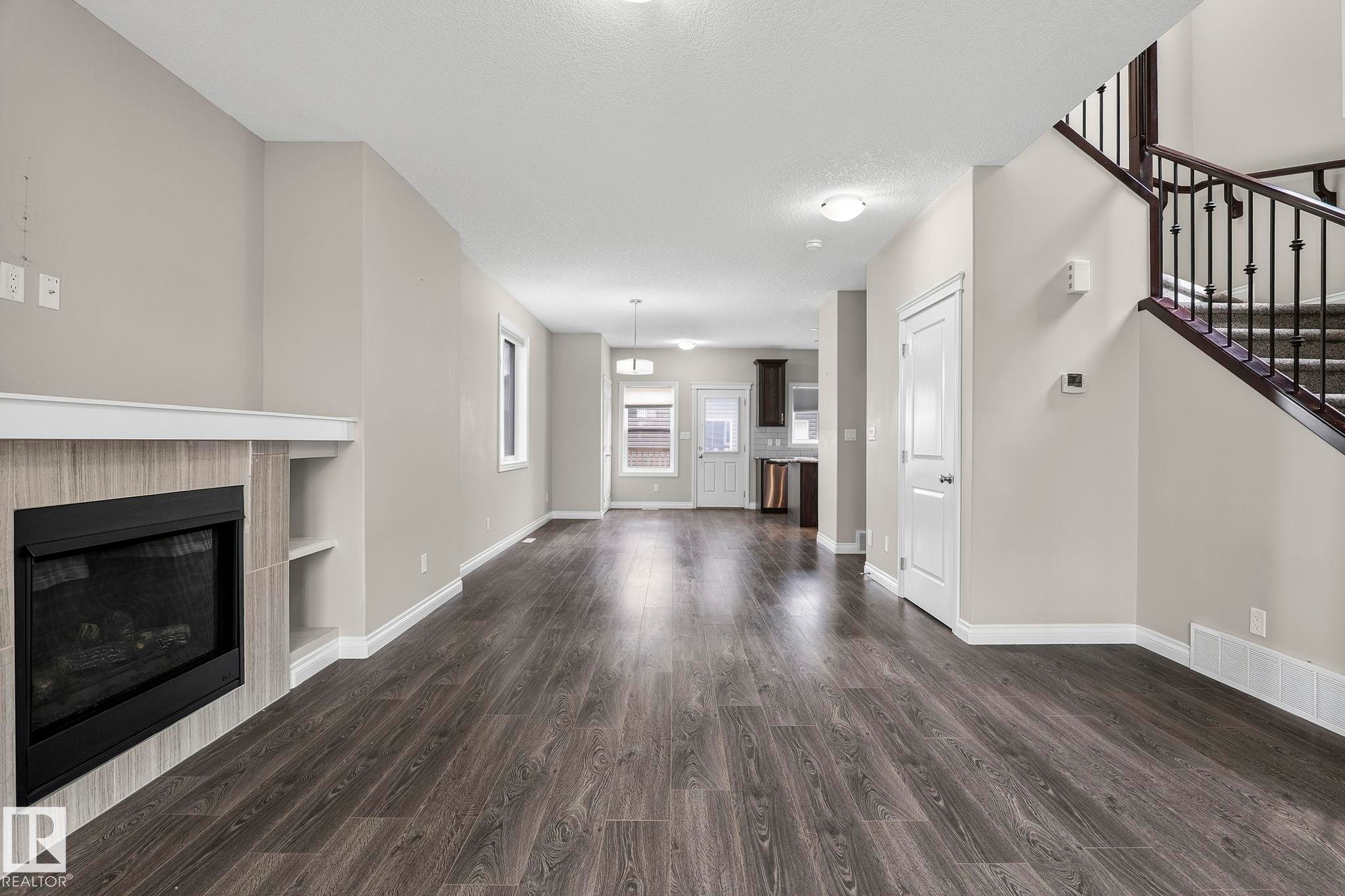 Open-concept living area featuring wood-finish flooring, a tiled fireplace with integrated shelving, and neutral wall tones - 6927 Cardinal Wynd Sw, Edmonton, AB - Indoor Photo Showing Living Room With Fireplace