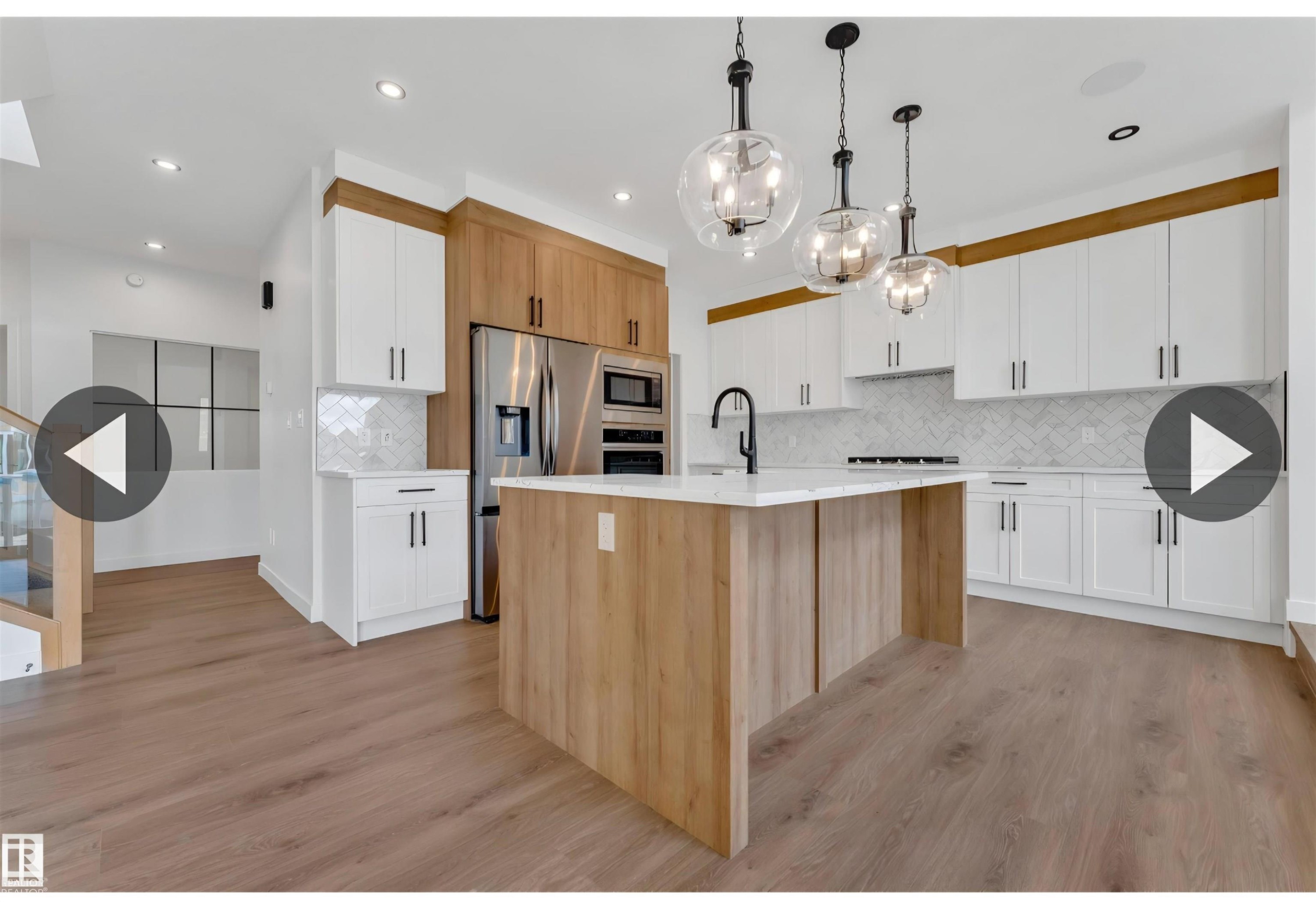 Modern kitchen featuring an island with a light wood-finish base and white countertop, white upper and lower cabinetry, and complementary wood-finish cabinetry - 13140 187 Avenue, Edmonton, AB