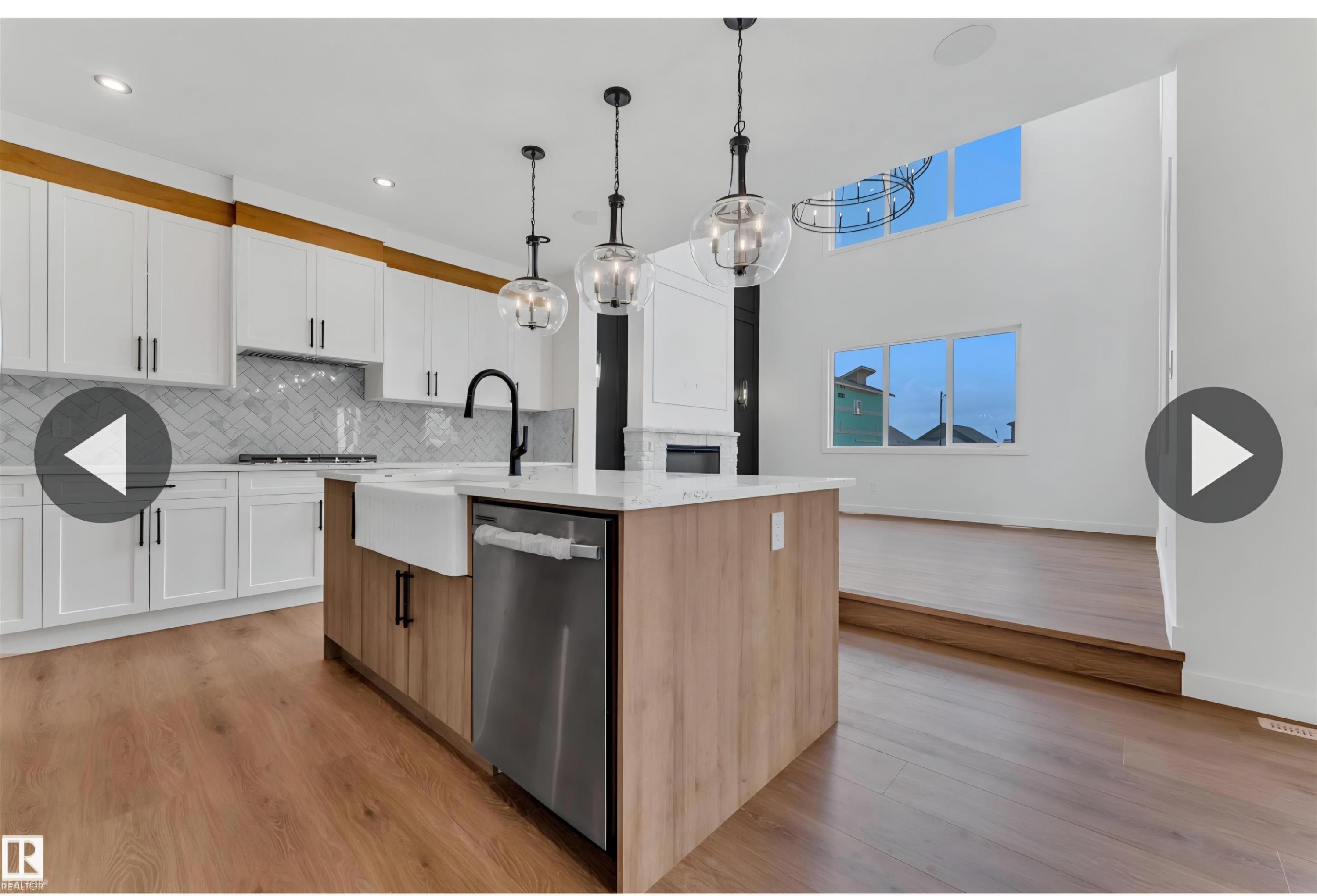 Modern kitchen featuring a large island with a farmhouse sink, stainless steel appliances, white cabinetry, and a herringbone tile backsplash - 13140 187 Avenue, Edmonton, AB