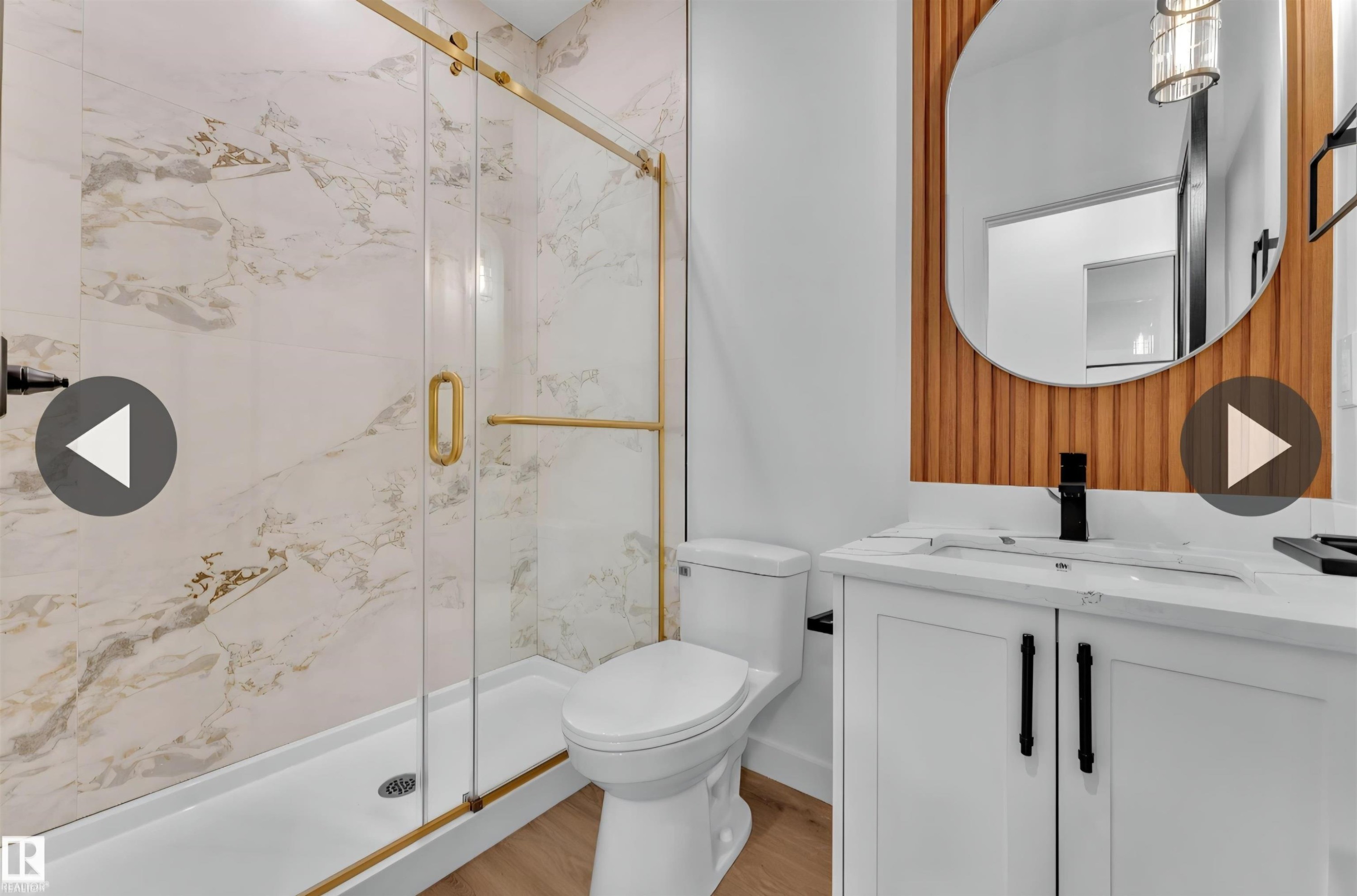 Modern bathroom featuring a glass shower with gold-tone hardware, white marble-look tile, wood-finish flooring, and a white vanity with black hardware - 13140 187 Avenue, Edmonton, AB