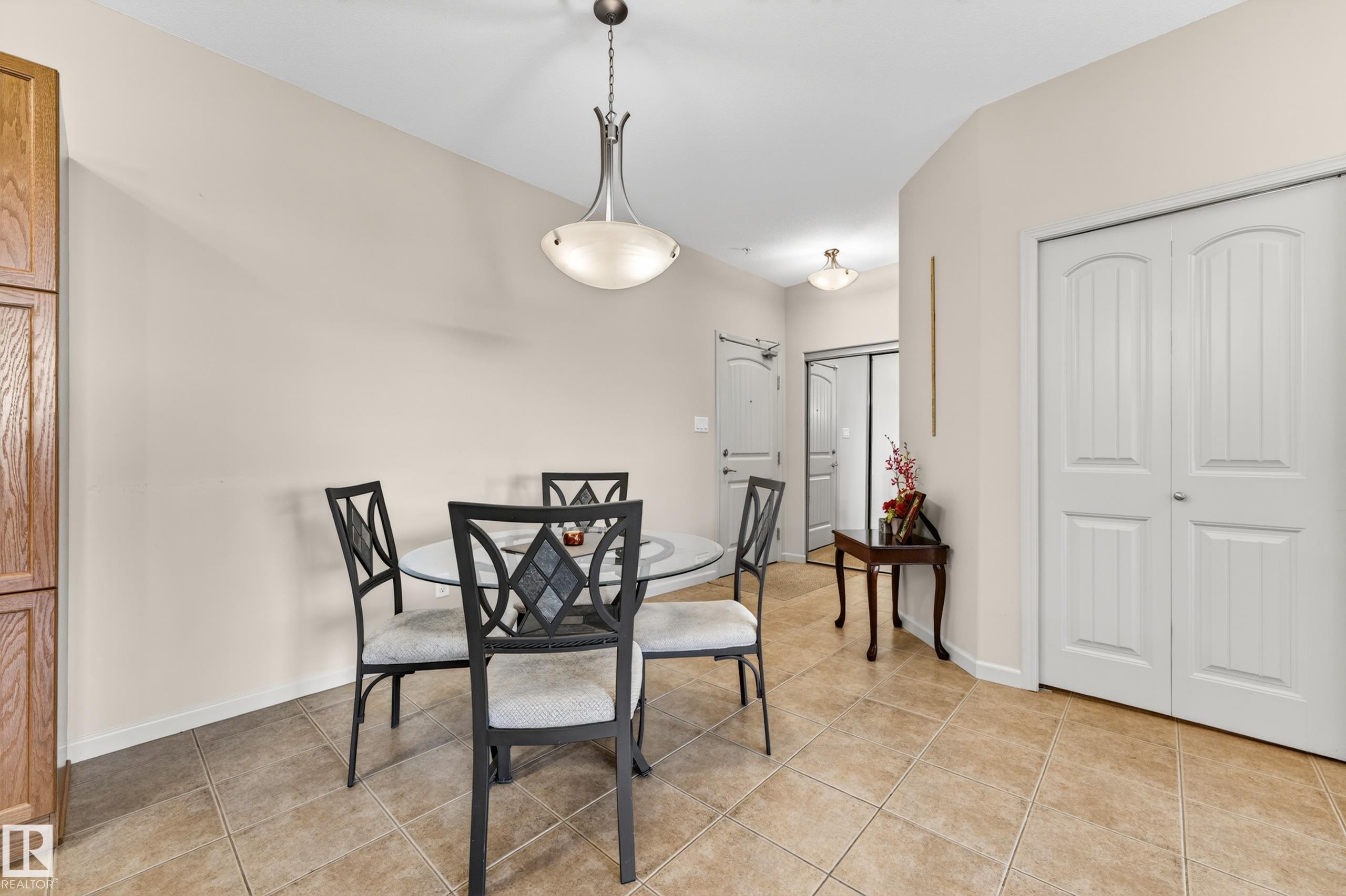 Dining area featuring neutral wall tones, tile flooring, a chandelier with frosted glass, and white bi-fold doors - 133 2503 Hanna Crescent, Edmonton, AB