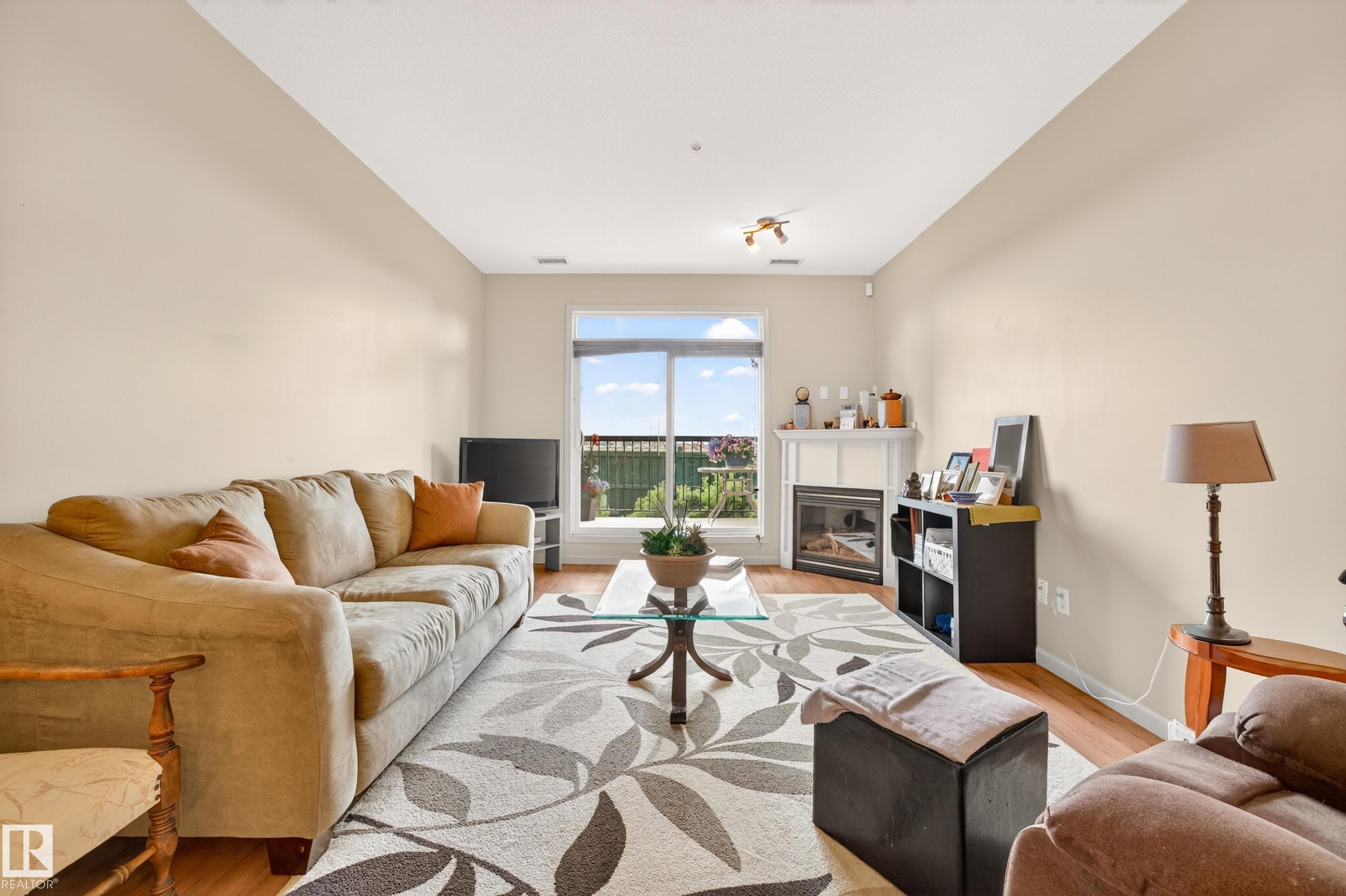 Living area featuring wood-finish flooring, a fireplace with a white mantel, and a large window with outdoor visibility - 133 2503 Hanna Crescent, Edmonton, AB