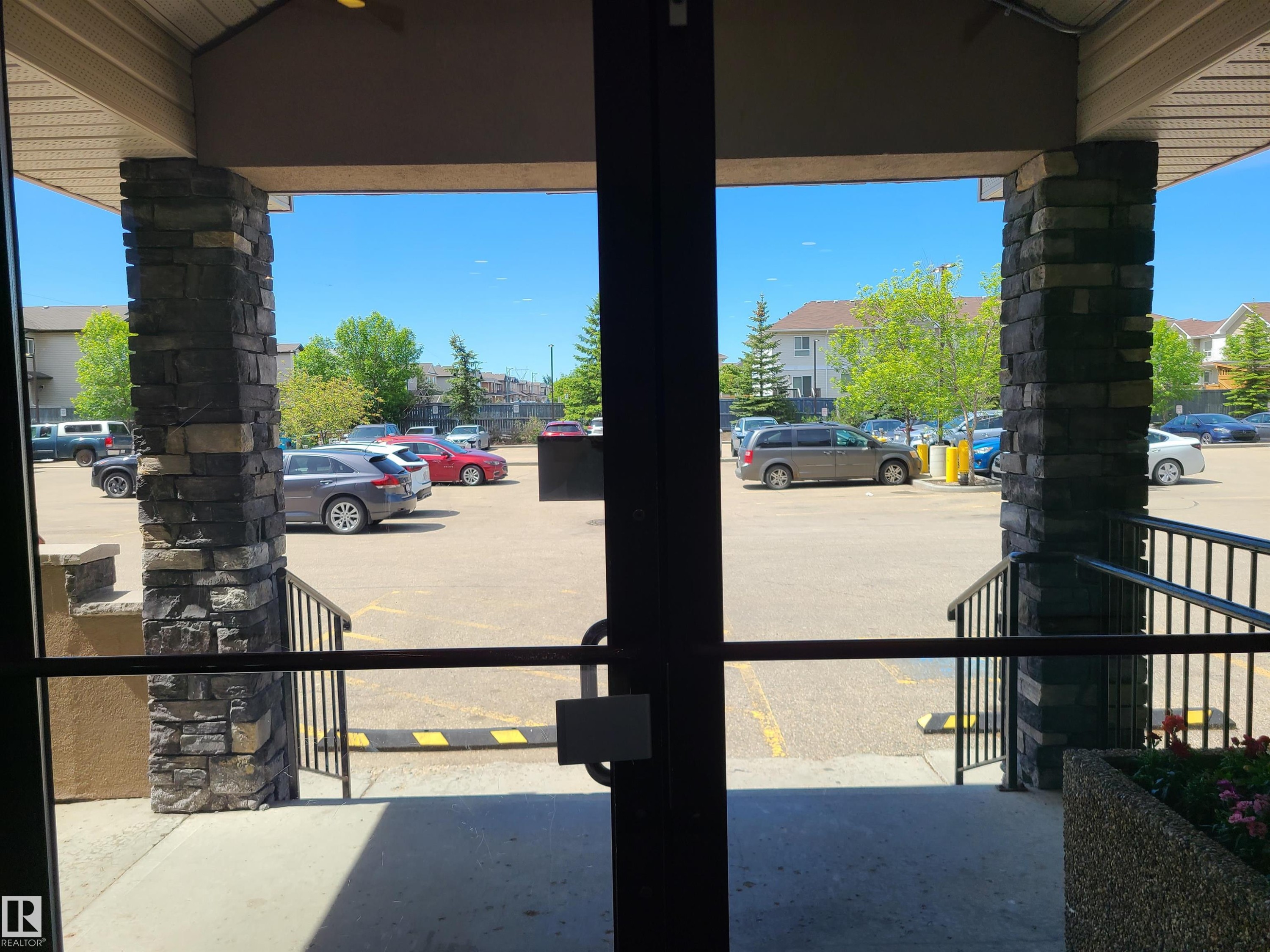 Stone-clad pillars framing an entryway with a black metal handrail and a planter - 116 5005 165 Avenue, Edmonton, AB
