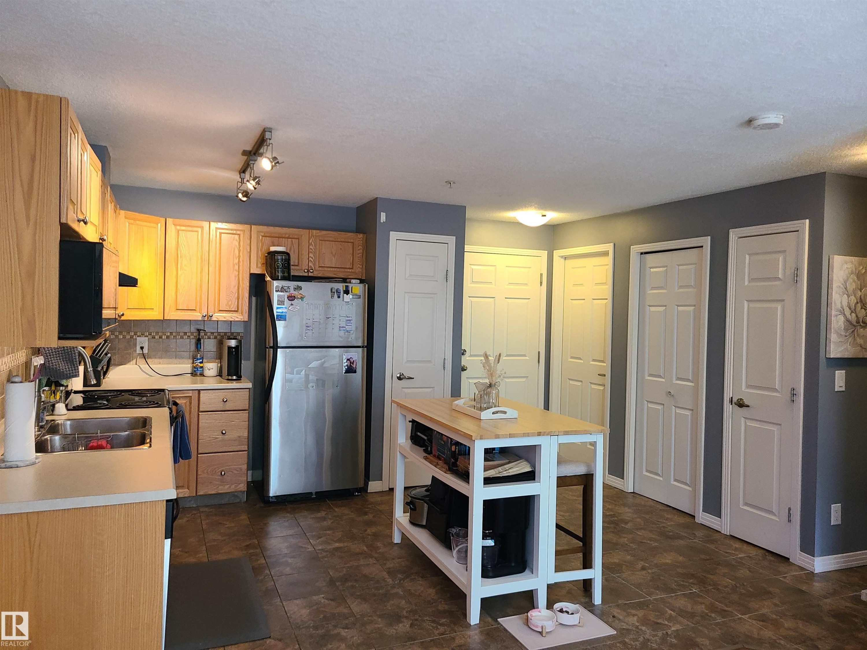 Kitchen featuring wood-finish cabinetry, stainless steel refrigerator, and a tiled backsplash - 116 5005 165 Avenue, Edmonton, AB