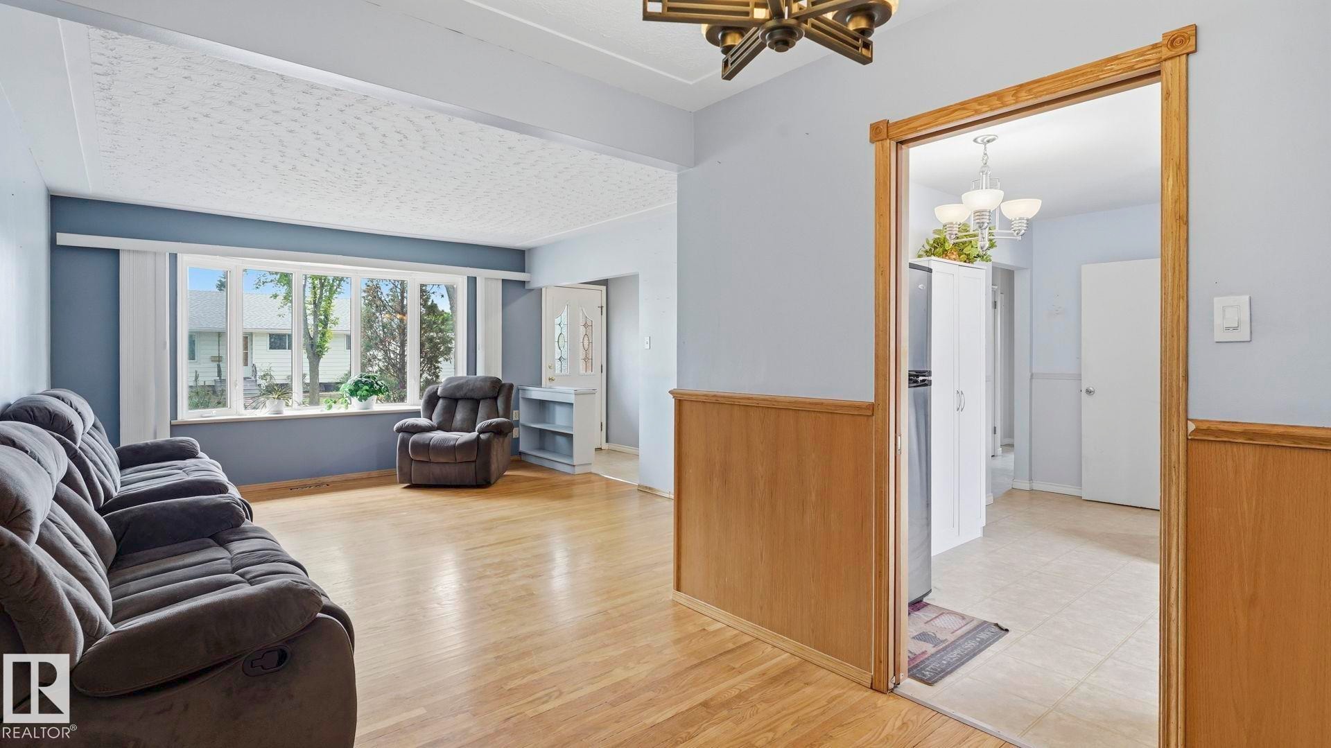 Living area featuring wood-finish flooring, a large bay window, and light blue wall paint - 13008 105 Street Nw, Edmonton, AB - Indoor