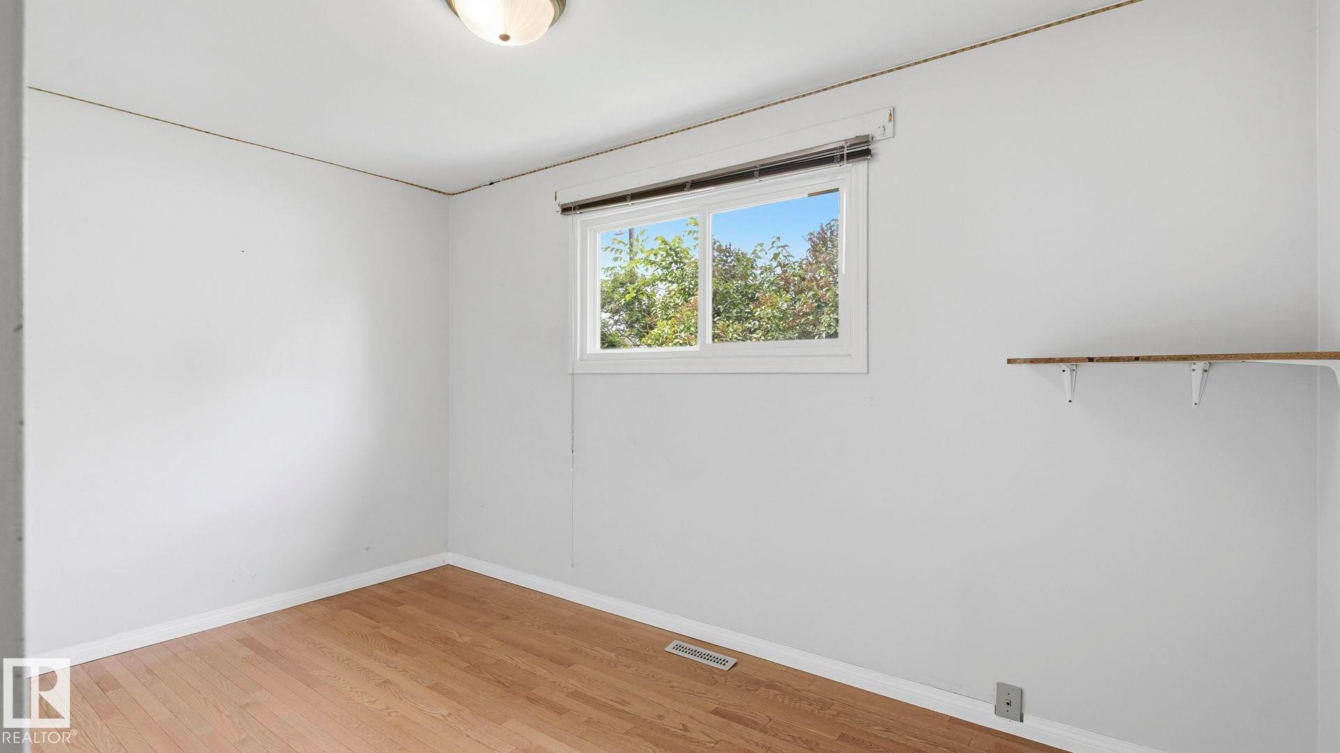 Room featuring wood-finish flooring, a white window frame, and a built-in shelving unit - 13008 105 Street Nw, Edmonton, AB - Indoor Photo Showing Other Room