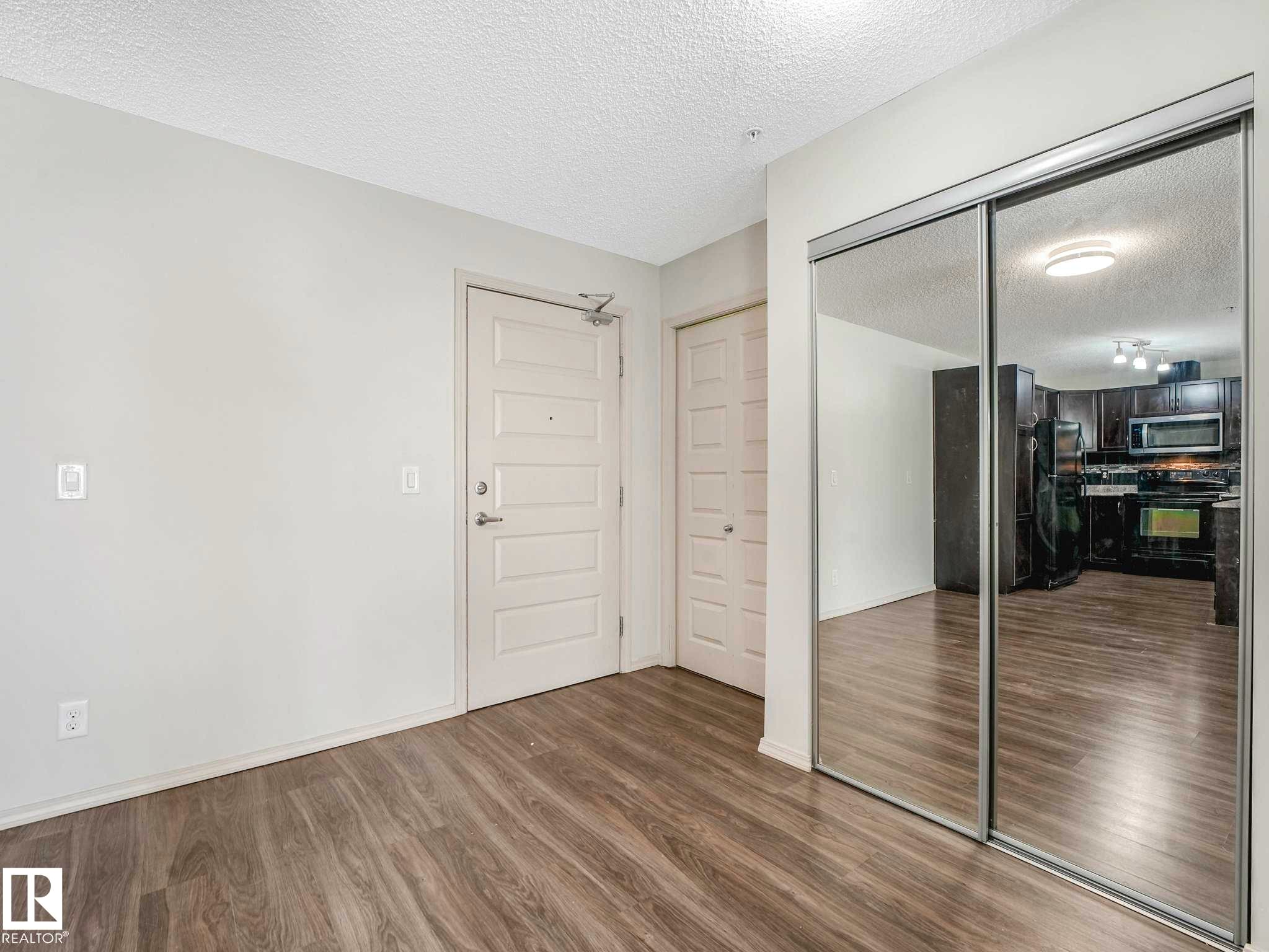 Wood-finish flooring throughout, featuring a five-panel entry door with brushed nickel hardware - 117 6070 Schonsee Way, Edmonton, AB