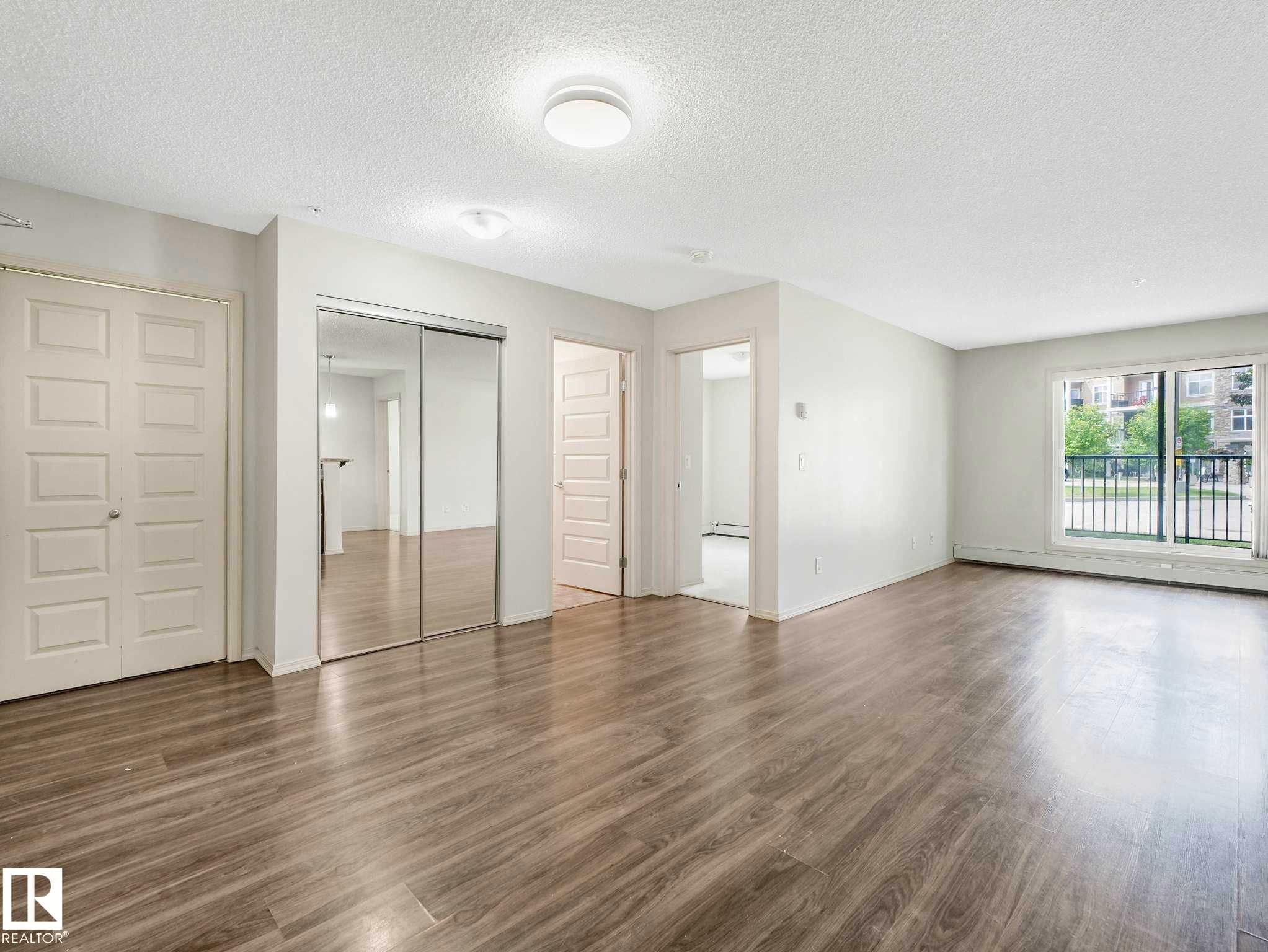 Spacious room featuring wood-finish flooring, white walls, and a sliding glass door providing external exposure - 117 6070 Schonsee Way, Edmonton, AB
