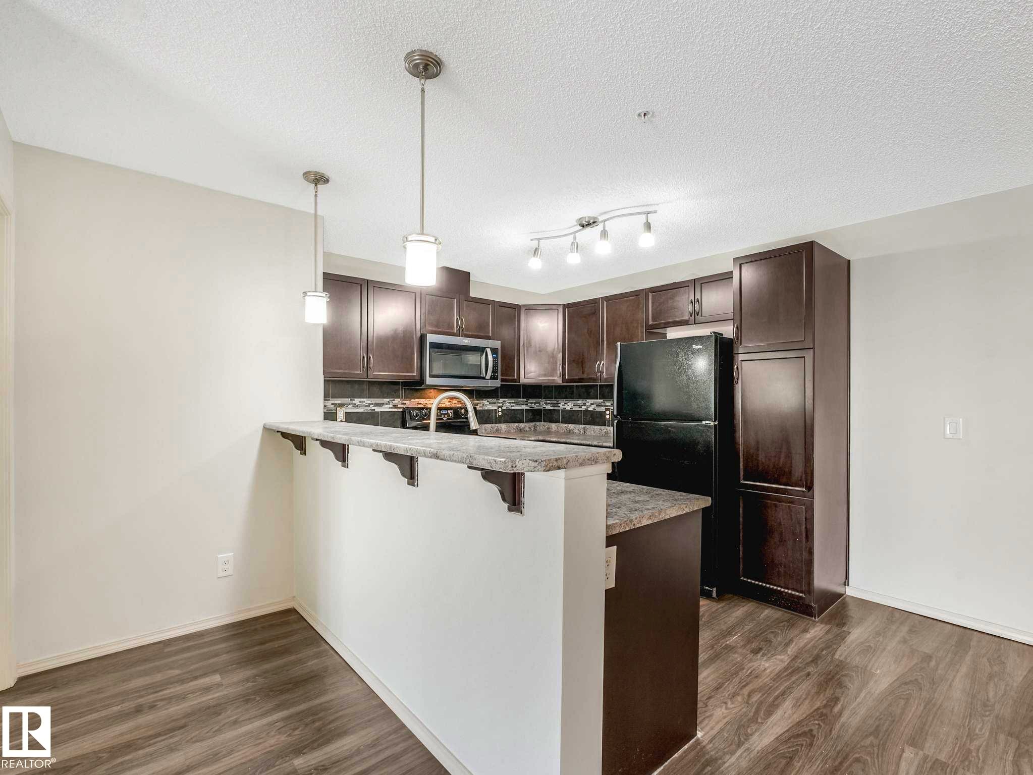 Kitchen featuring wood-finish flooring, dark cabinetry, and stone-look countertops - 117 6070 Schonsee Way, Edmonton, AB