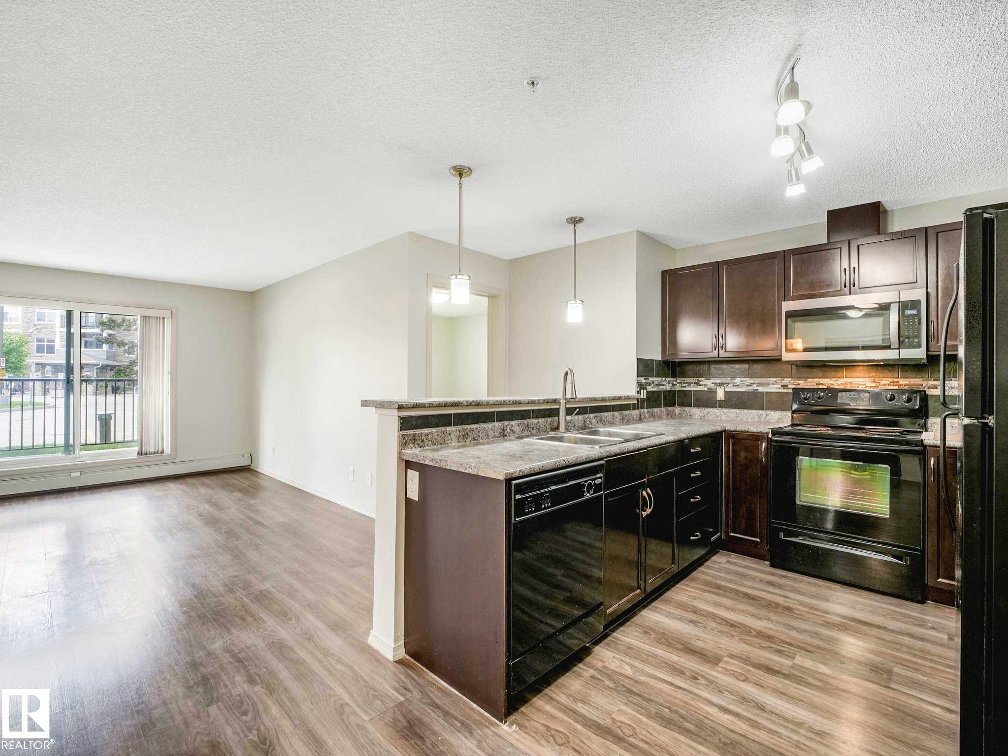 Kitchen featuring wood-finish flooring, dark cabinetry, and black appliances - 117 6070 Schonsee Way, Edmonton, AB