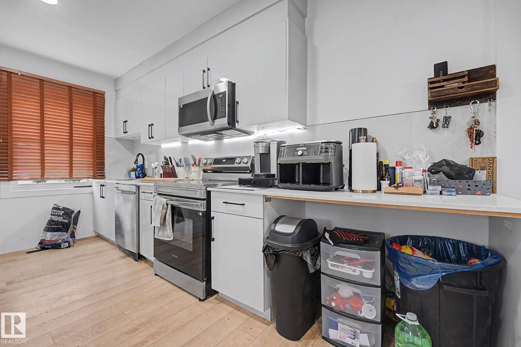 Modern kitchen featuring white cabinetry, stainless steel appliances, light wood-finish flooring, and white countertops - 11914 124 Street, Edmonton, AB