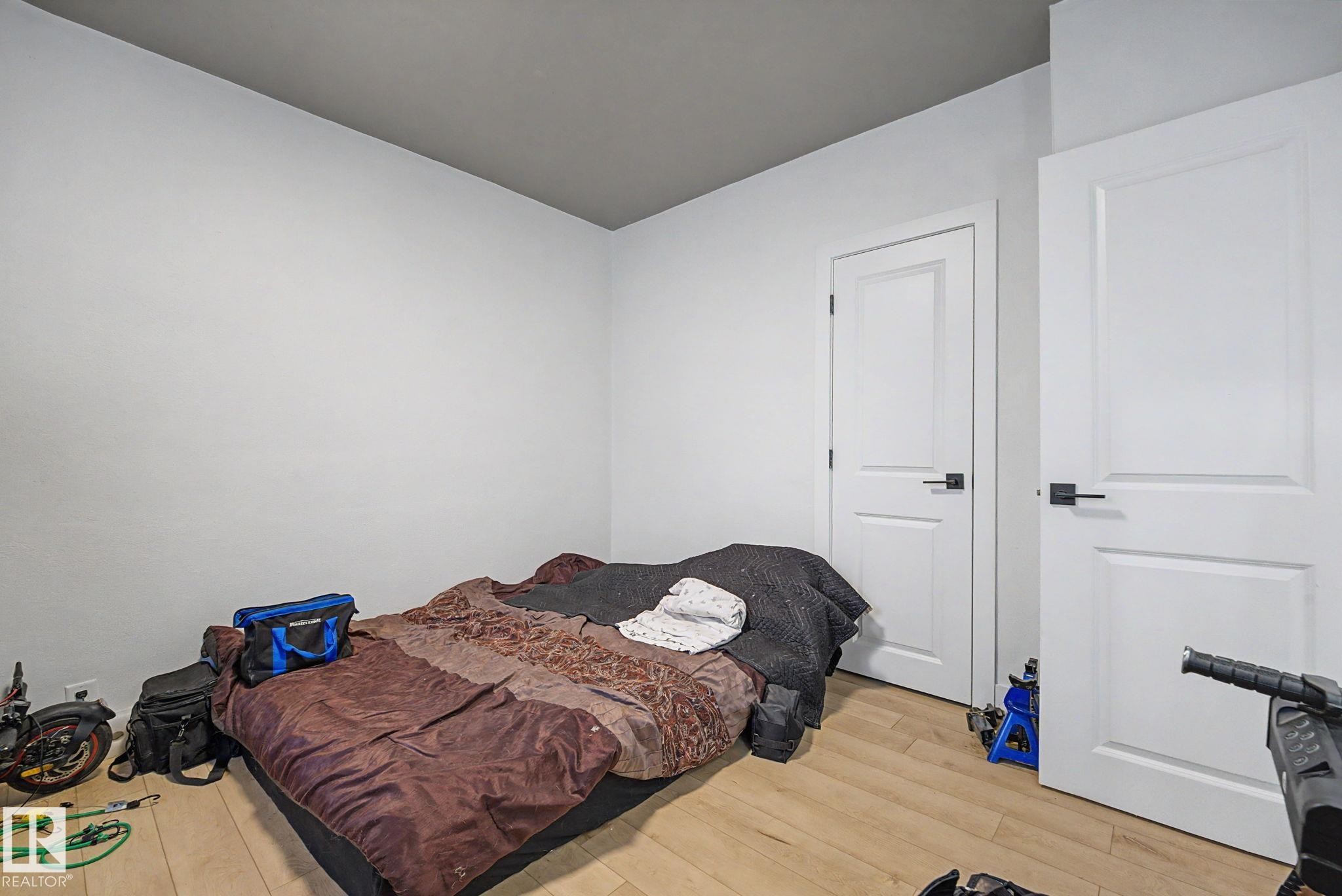 Room featuring light wood-finish flooring, two white panel doors with black hardware, white walls, and a dark ceiling - 11914 124 Street, Edmonton, AB