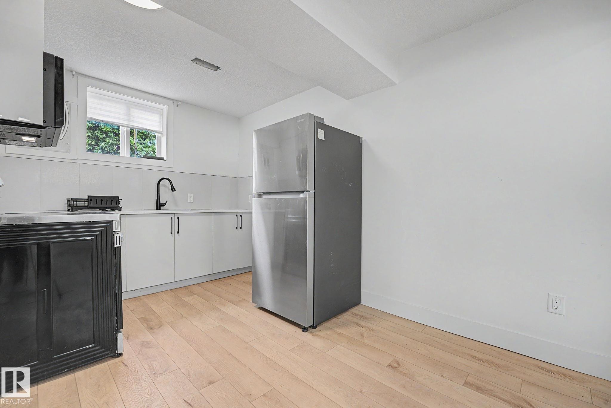 Kitchenette featuring light wood-finish flooring, white walls, and a stainless steel refrigerator - 11914 124 Street, Edmonton, AB